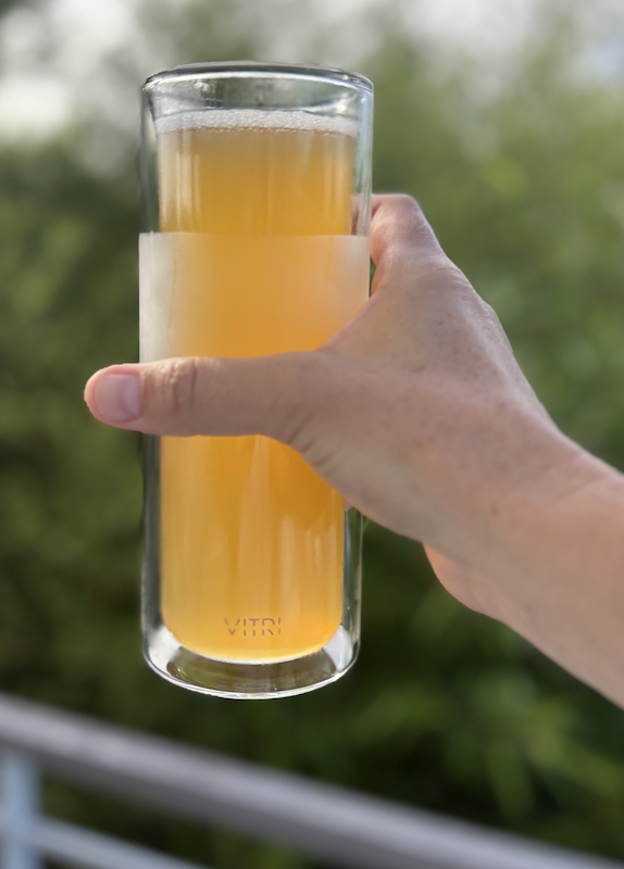 Outstretched arm holding a tall clear glass filled with fizzy beer