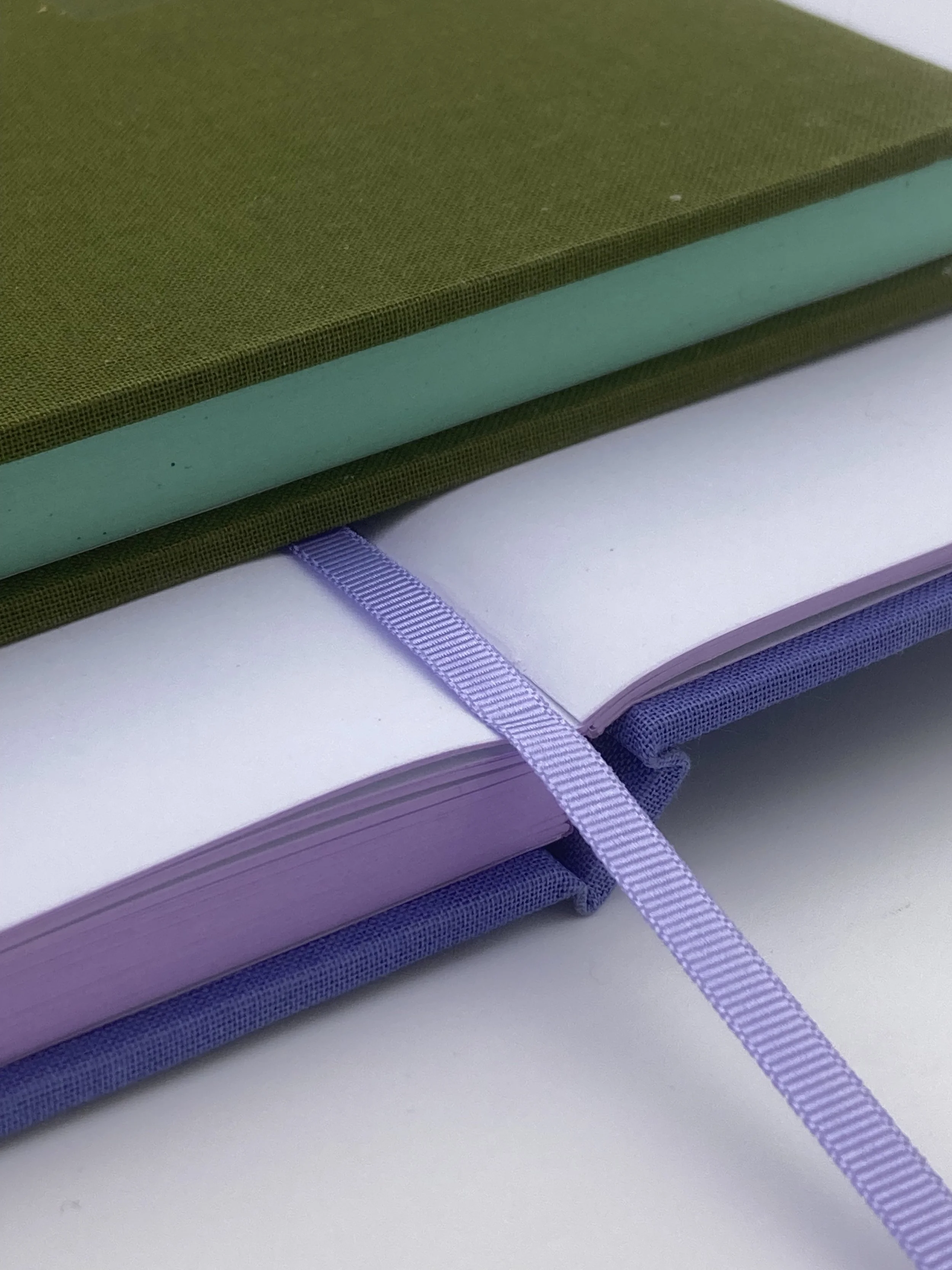 A purple ribbon sits flatly upon the lavender pages of a notebook. 