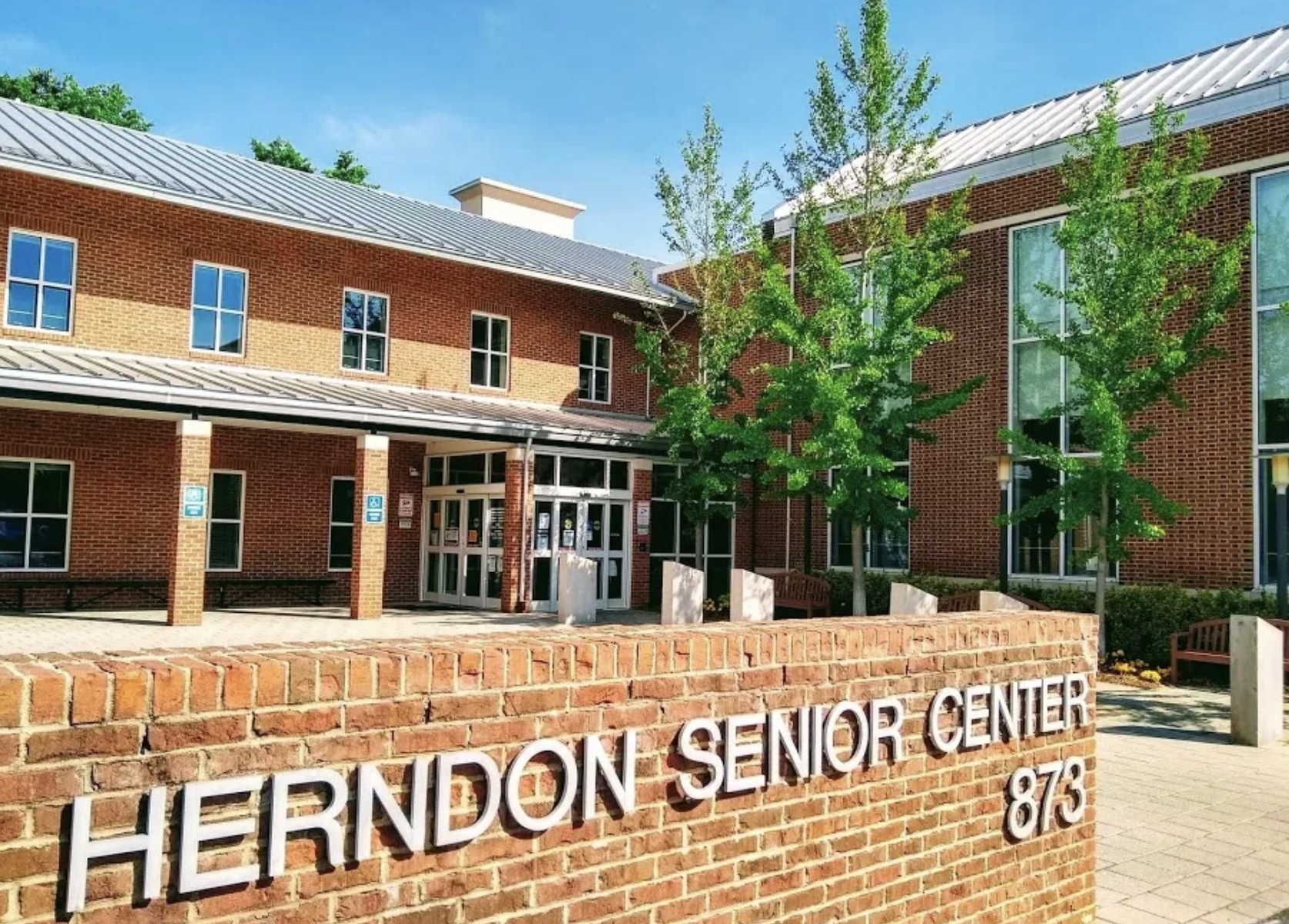 Exterior view of the Herndon Senior Center building with a brick sign in the foreground and trees around the entrance.