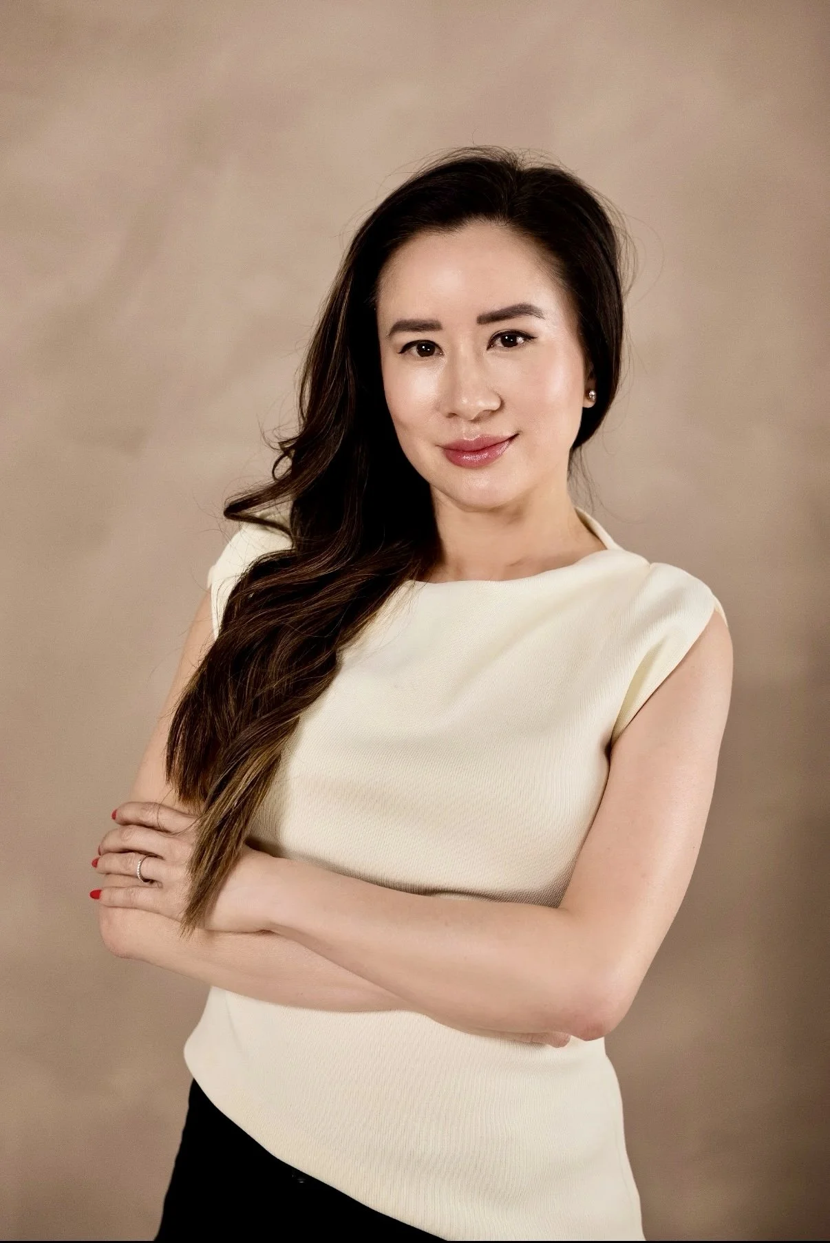 Professional woman with long wavy hair smiling outdoors, wearing a black blazer and beige blouse.