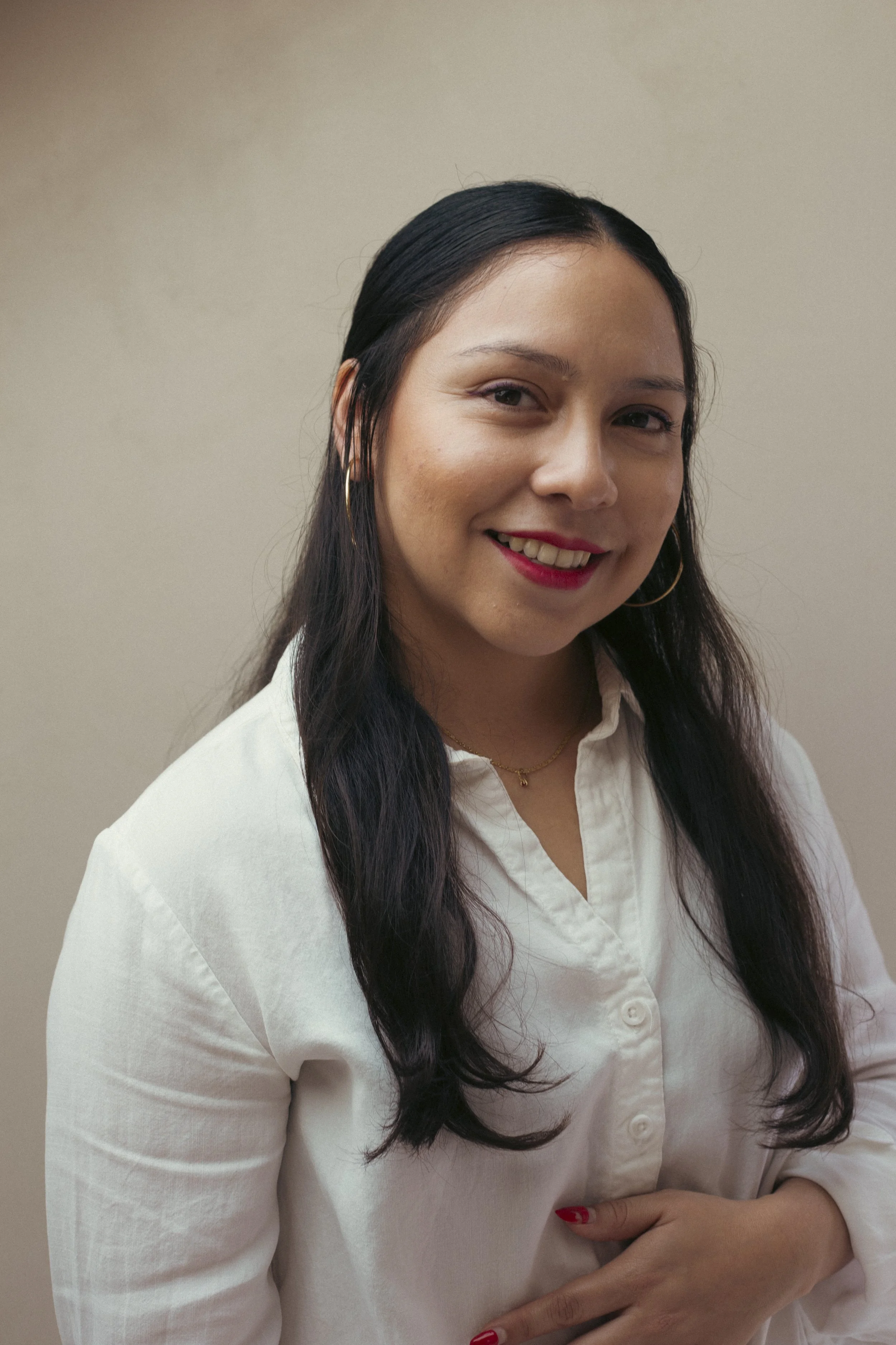 Portrait of a smiling woman with wavy light brown hair, standing against a plain gray wall.