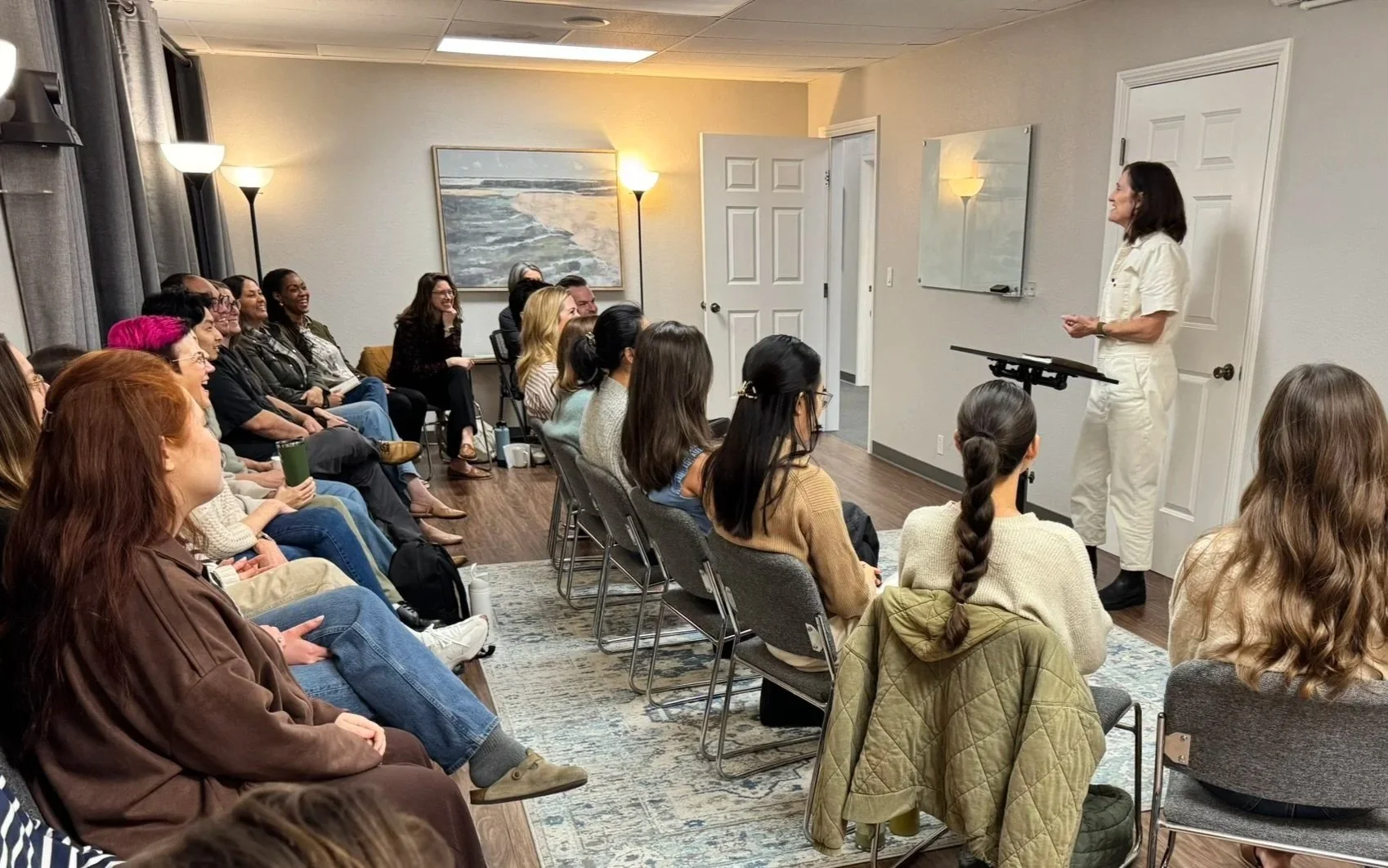 A woman giving a presentation to a seated group of diverse adults in a conference room.