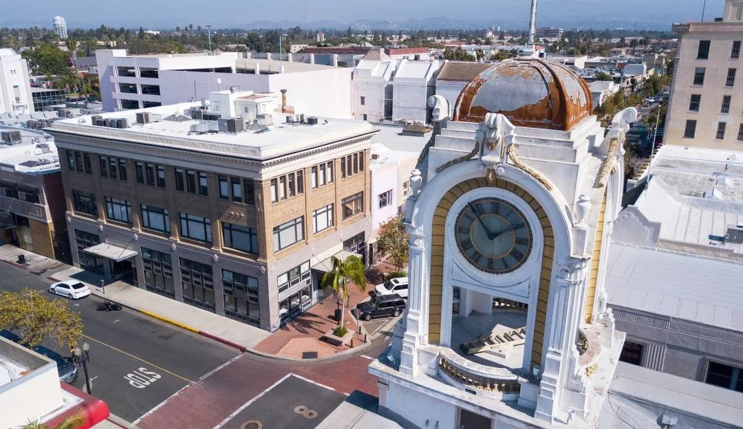 An aerial view of a historic clock tower on a city street with buildings and cars, under a clear sky.