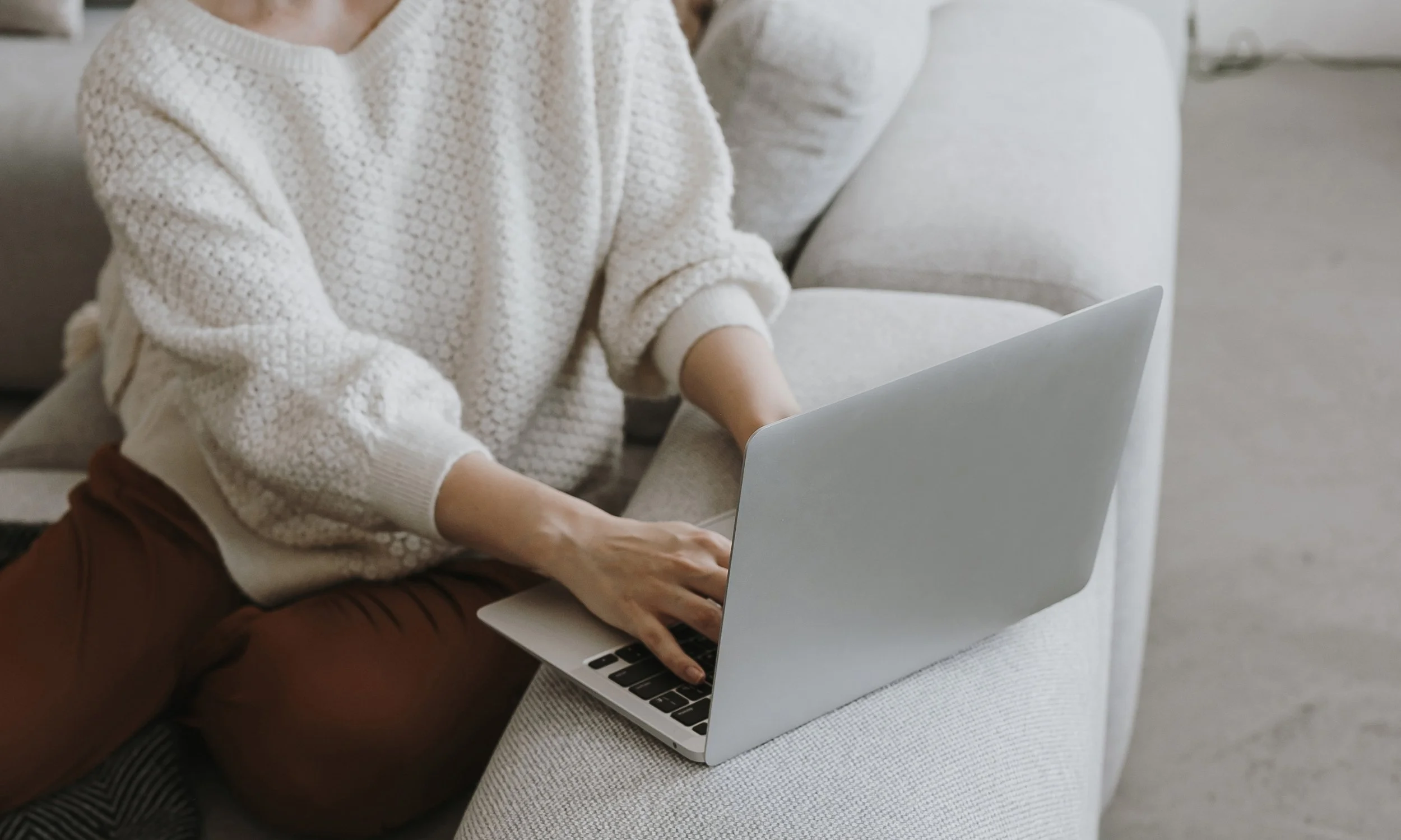 Person working on a laptop while sitting on a sofa.