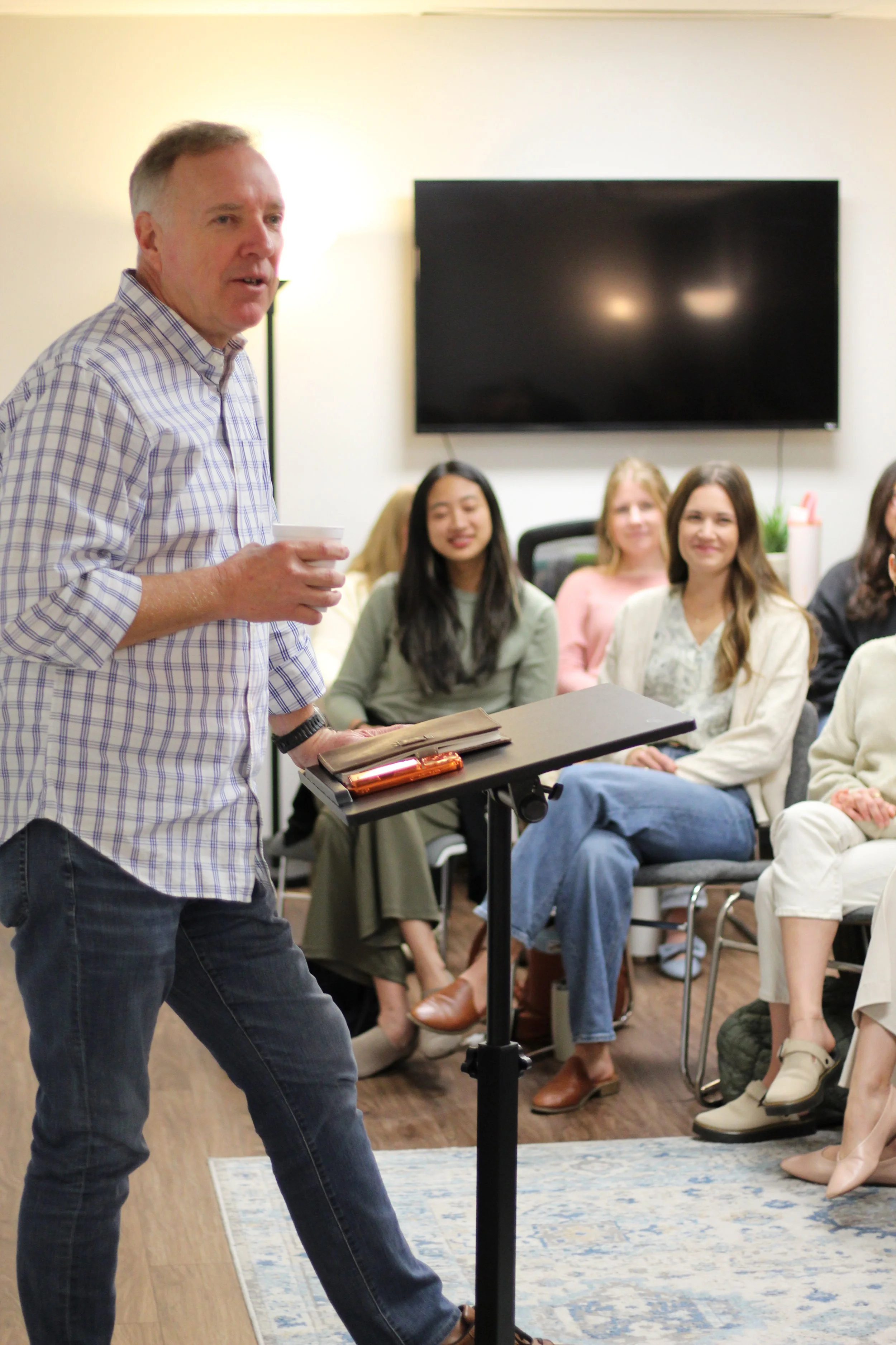 Man giving a presentation to a group of women seated in a conference room.