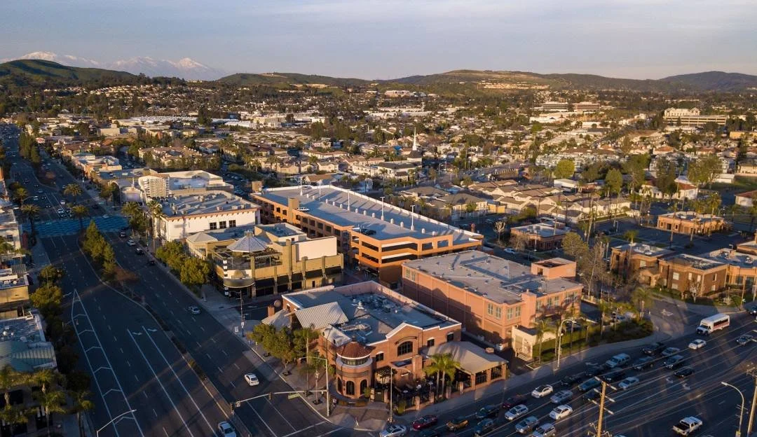 Aerial view of a cityscape with commercial buildings, streets, cars, and mountains in the background.