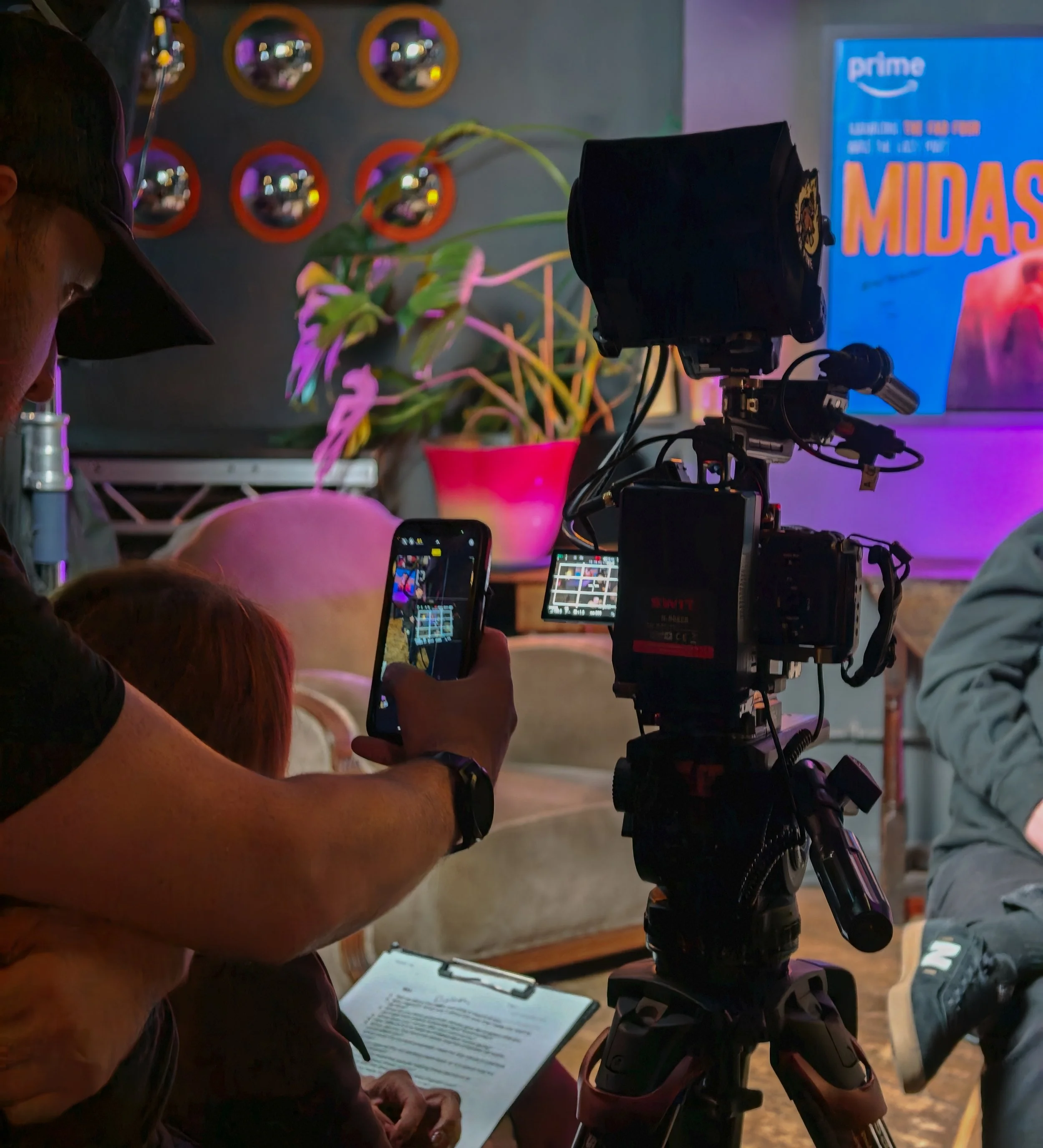 A person adjusting camera equipment during a presentation or filming session, with a tablet and audience in the background.