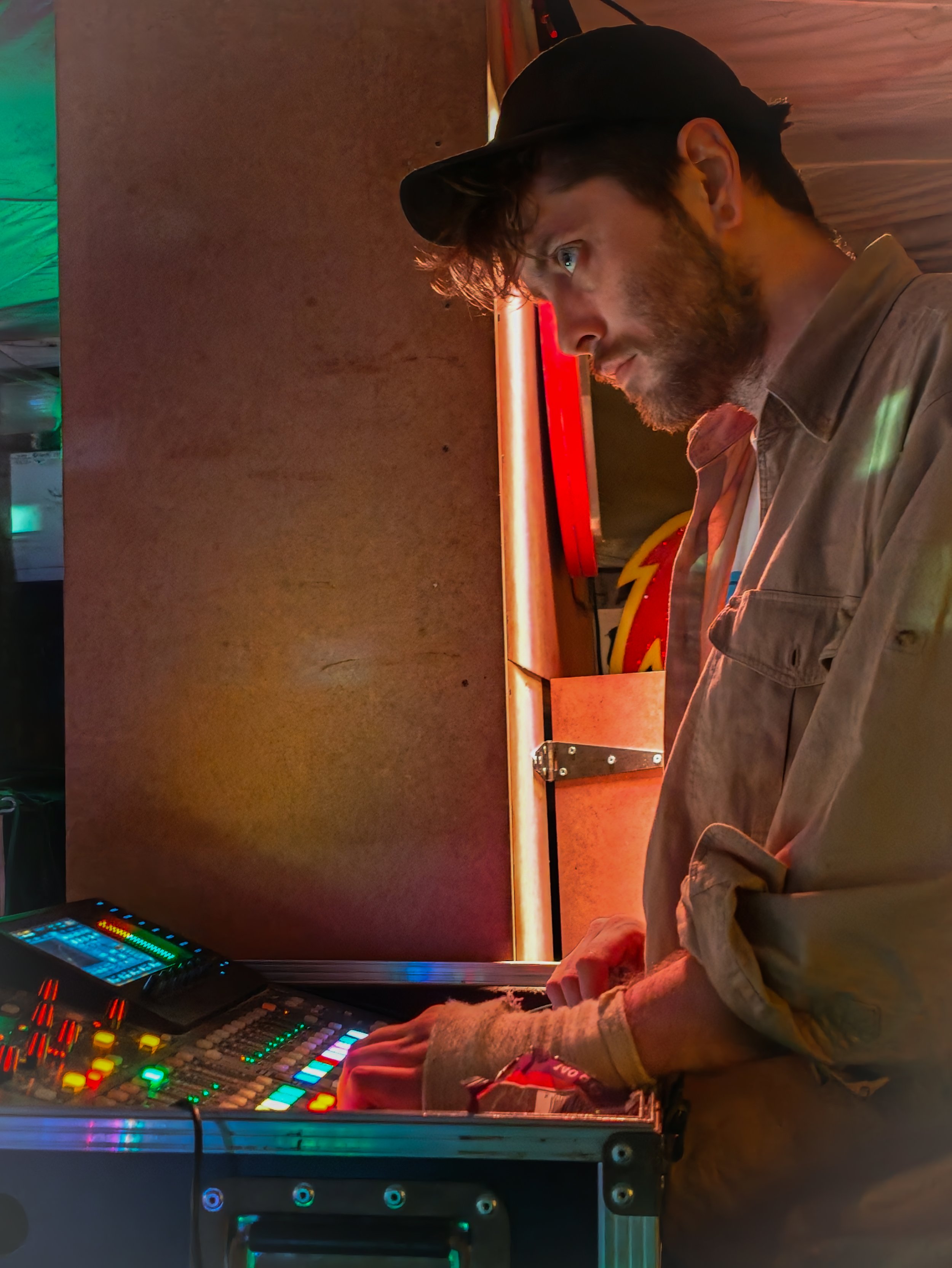 A man playing using a sound desk with colourful lights in a dimly lit indoor setting.