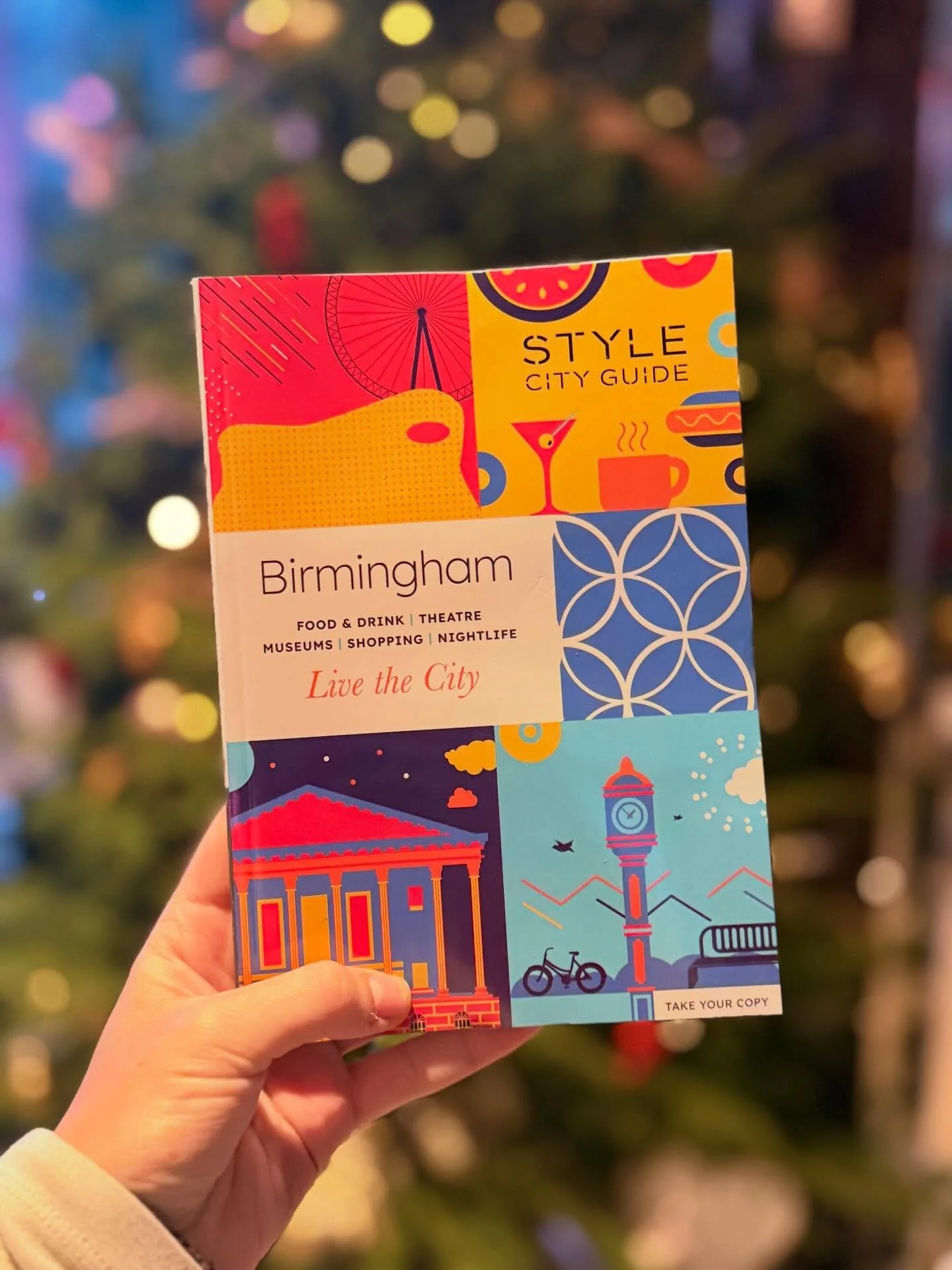 Colorful Birmingham city guide brochure held up in front of a decorated Christmas tree with blurred lights in the background.