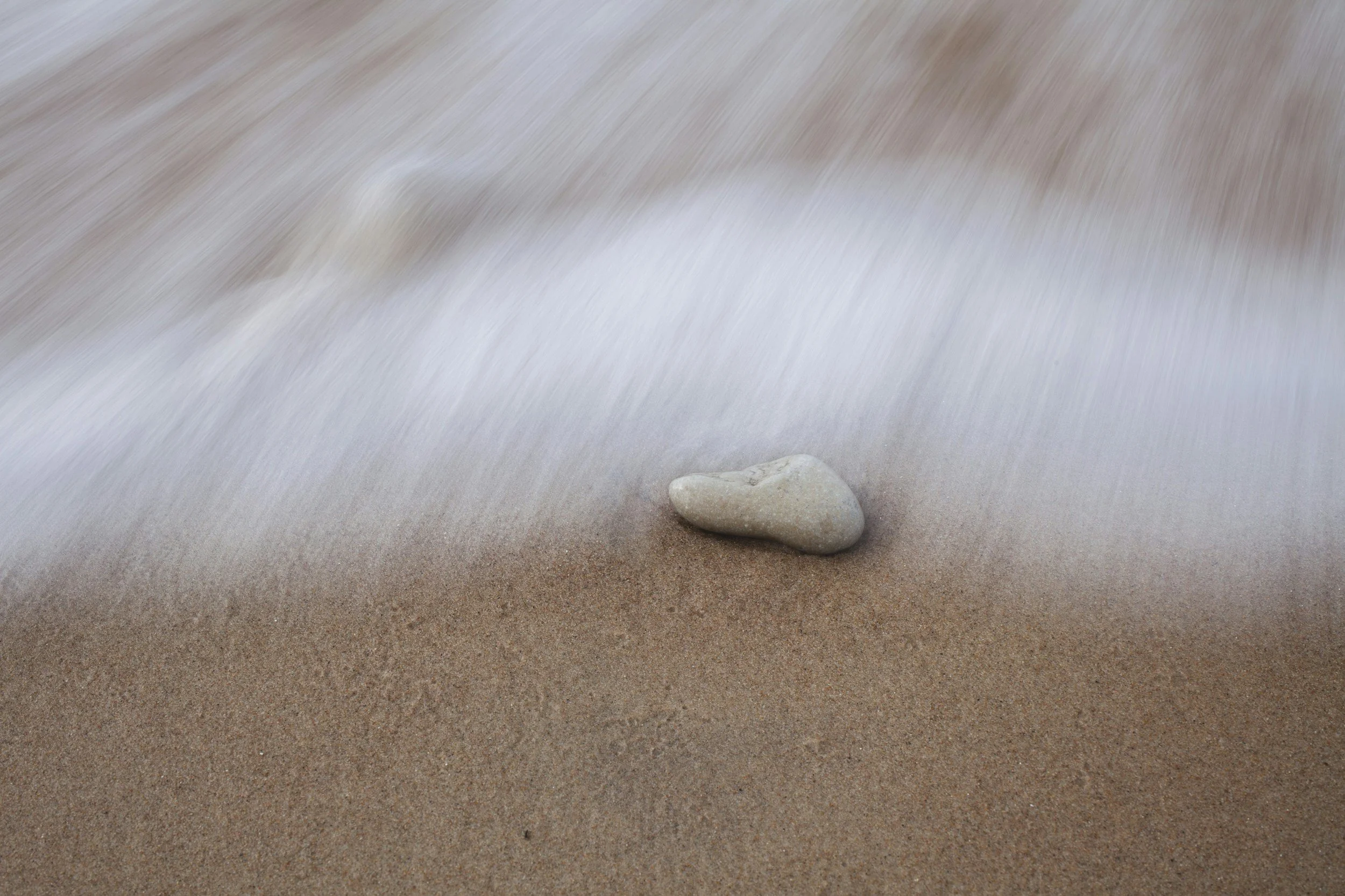 Individual: Small stone in shallow water, sand rippling around it.