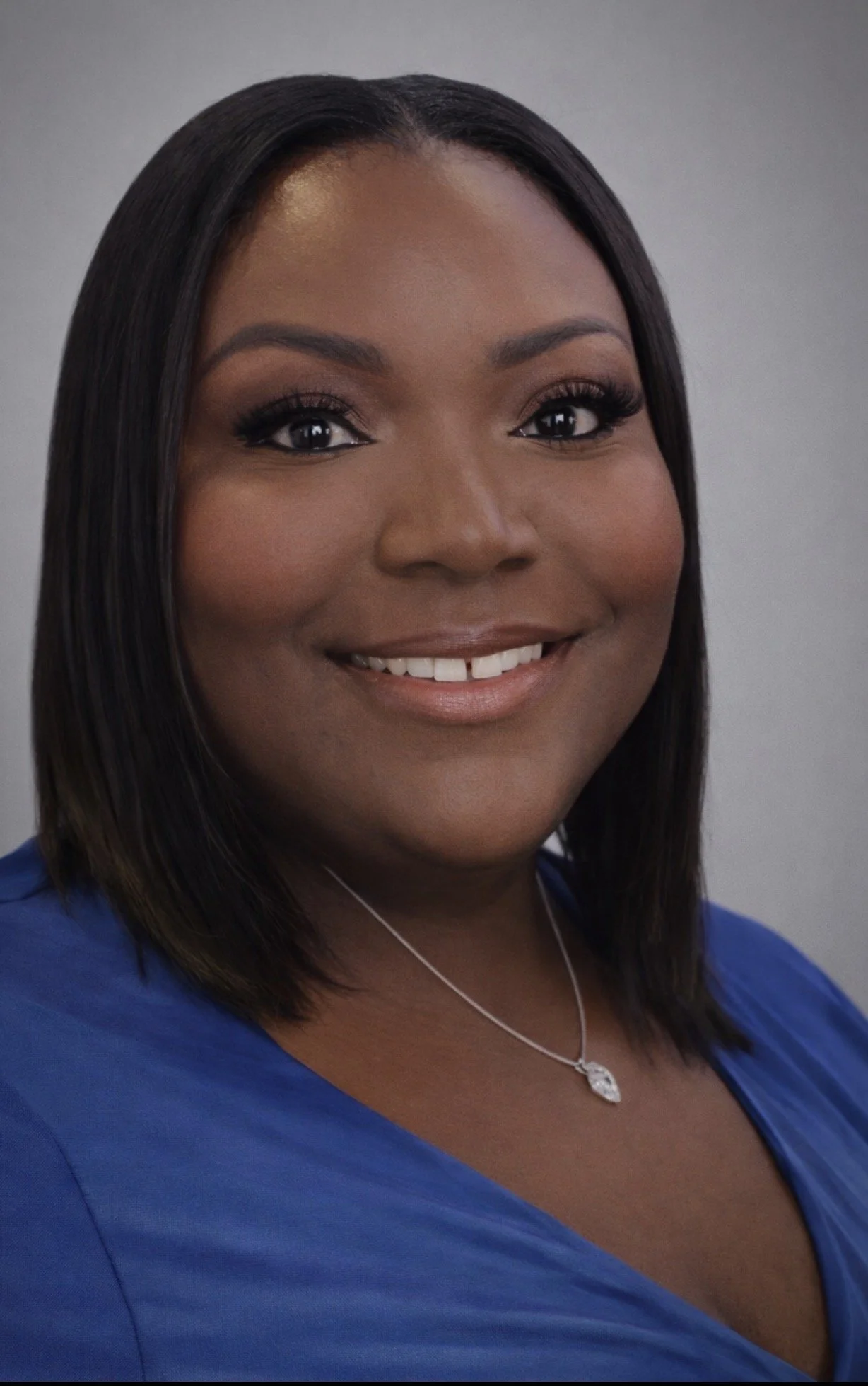 Woman with long braids wearing a pink top and black blazer standing outdoors in front of a glass building.