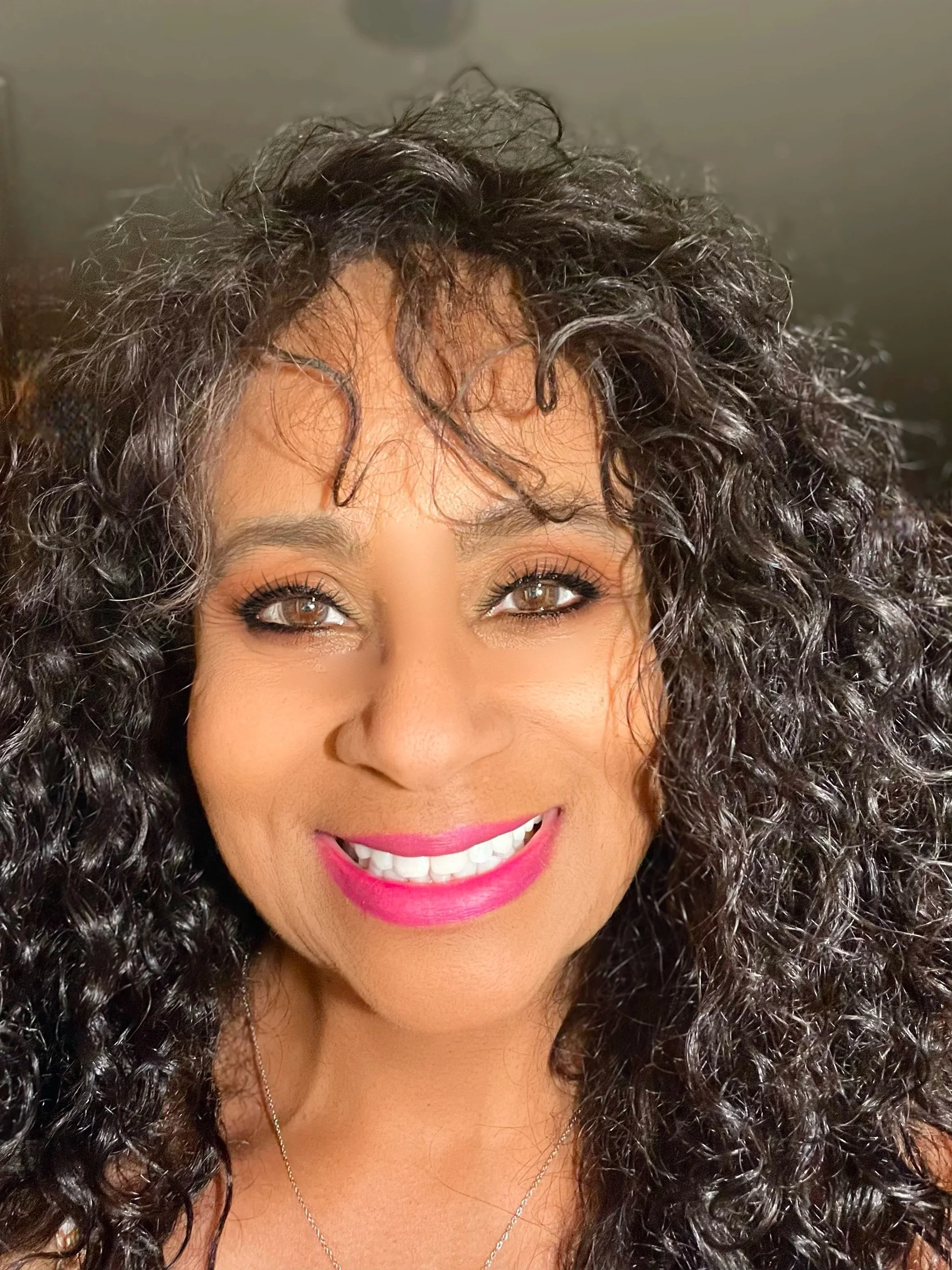 Headshot of a smiling woman with dark curly hair, wearing a blue shirt.