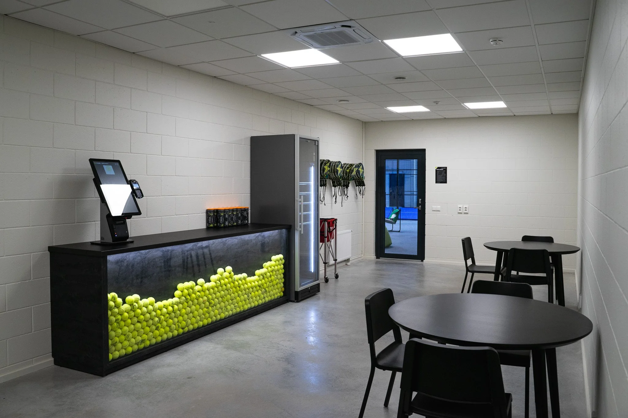 Indoor room with tables and chairs, tennis ball storage with tennis balls, vending machine, and golf bags