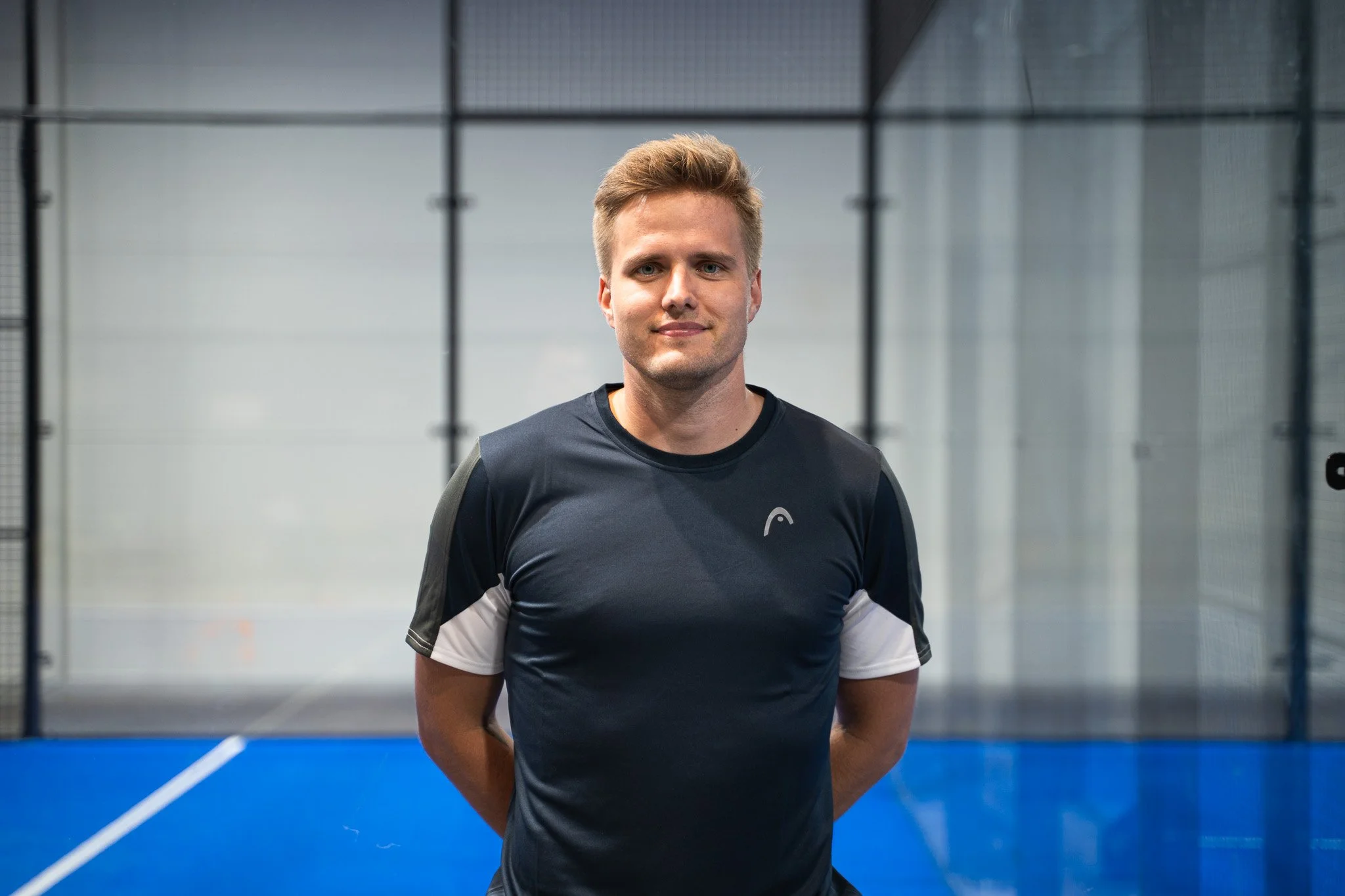 A young man with light brown hair in a sports shirt standing on an indoor sports court.