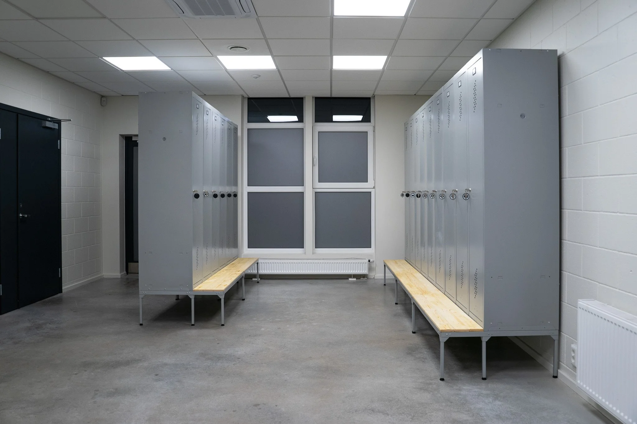 Empty locker room with metal lockers, wooden benches, and a window.