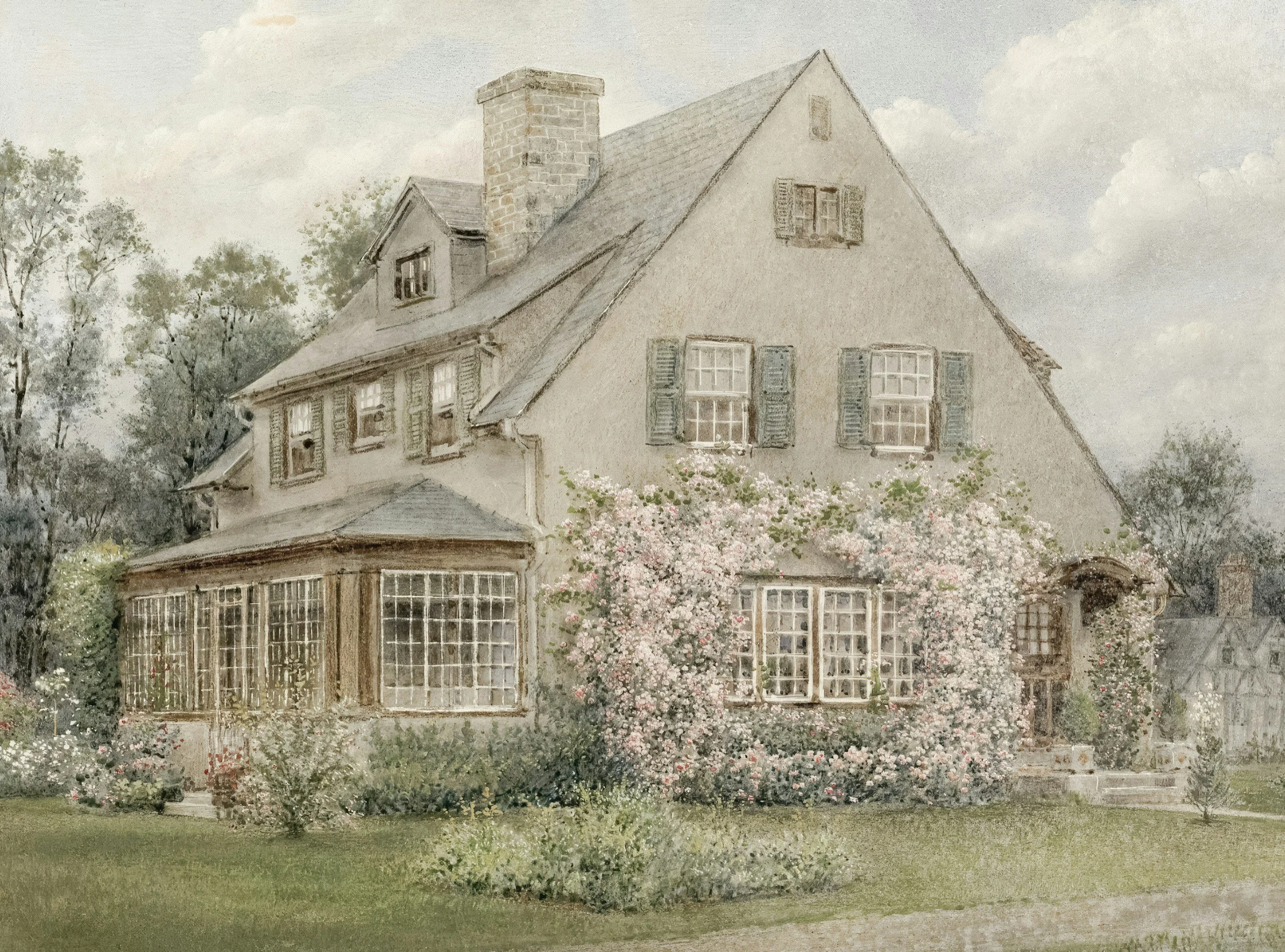 A large, vintage-style house with multiple stories, a steep roof, and numerous windows surrounded by flowering bushes and trees.