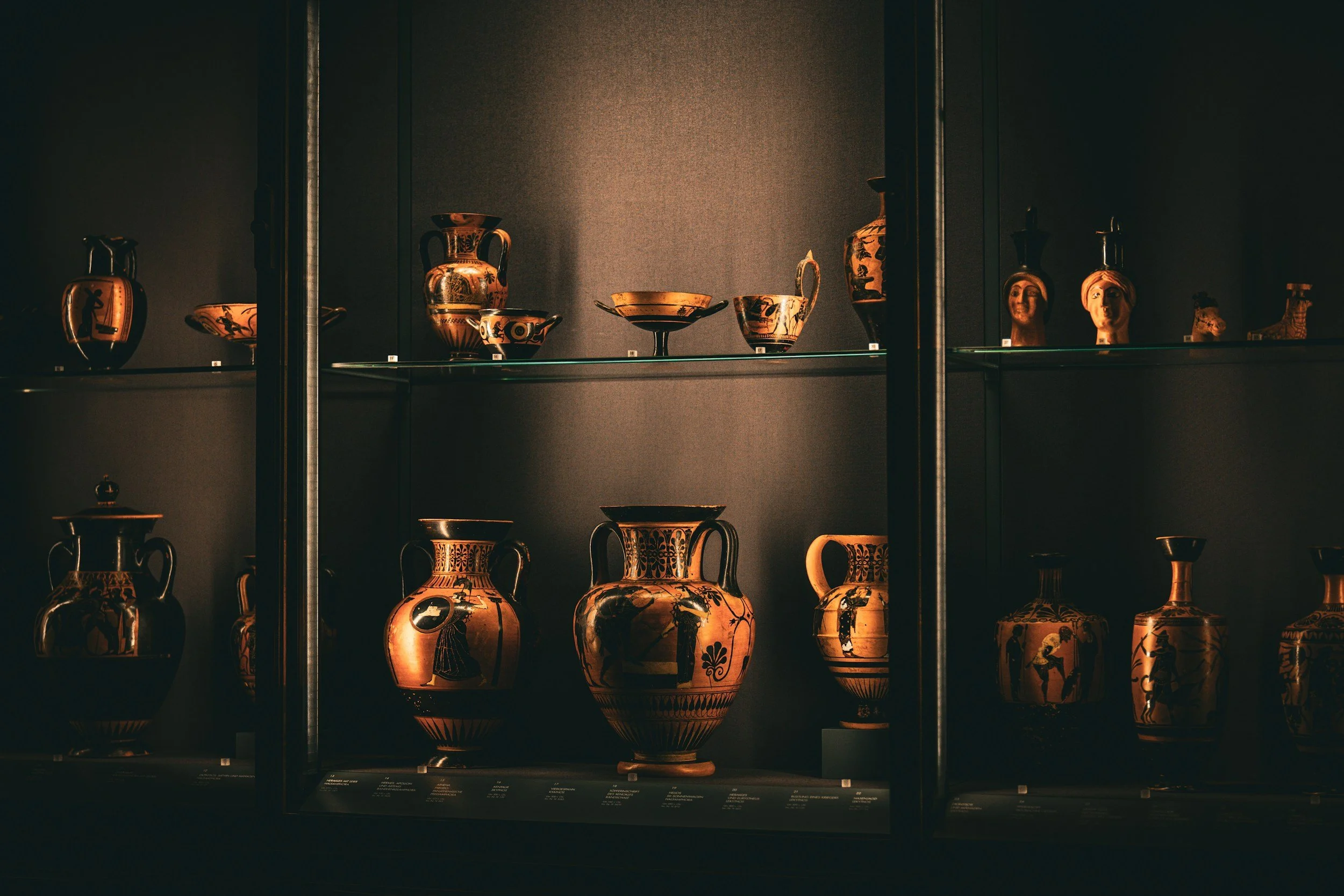 Ancient Greek pottery and vases displayed in a museum glass case.