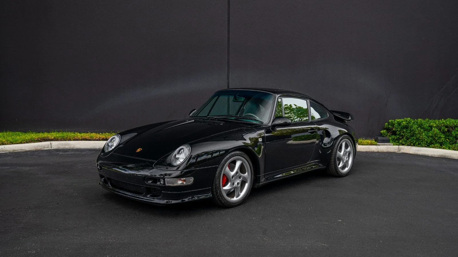 Black Ford Mustang sports car parked on a street near a river with bridge in the background, during daytime.
