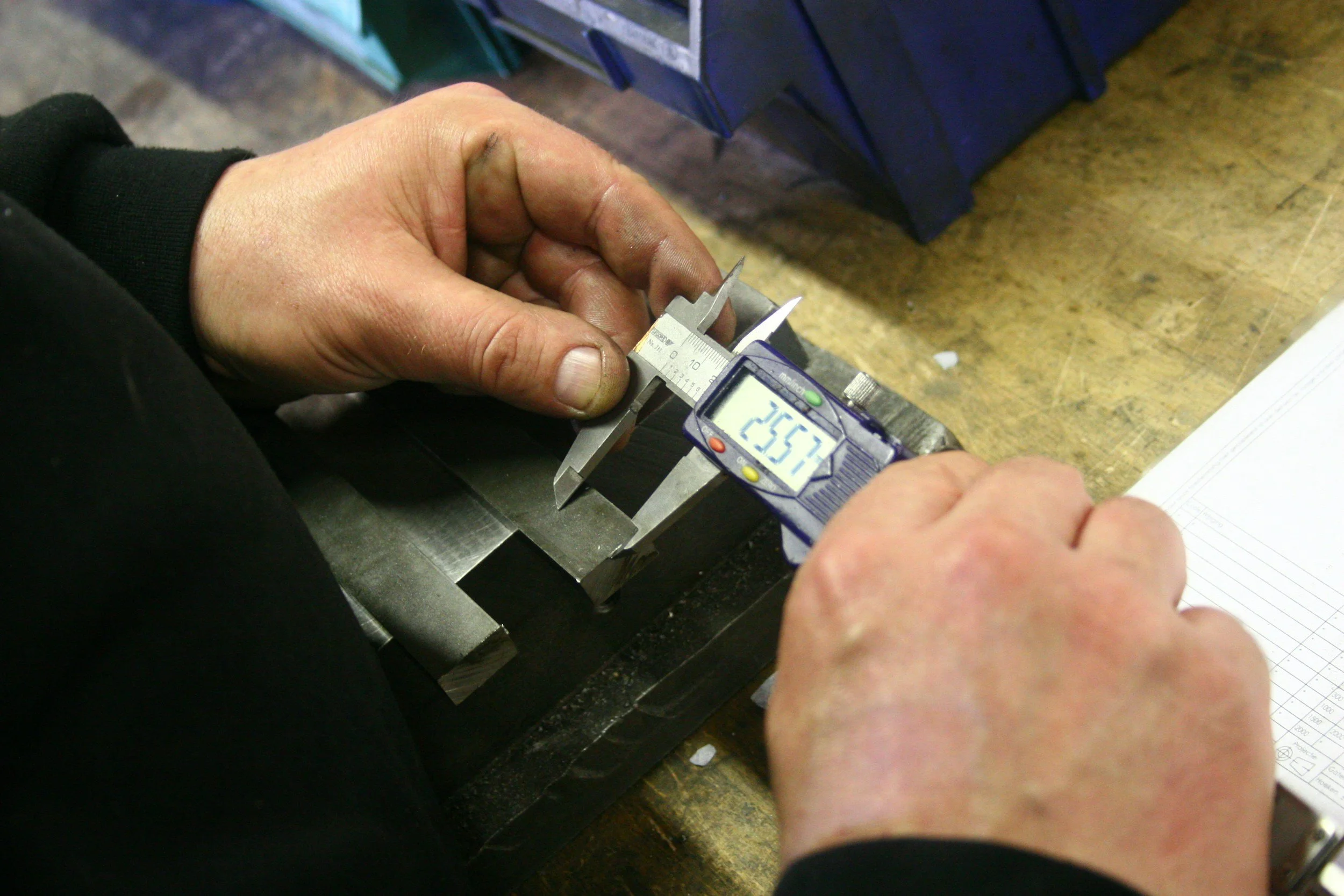Person using a digital caliper to measure a metal piece on a workbench.