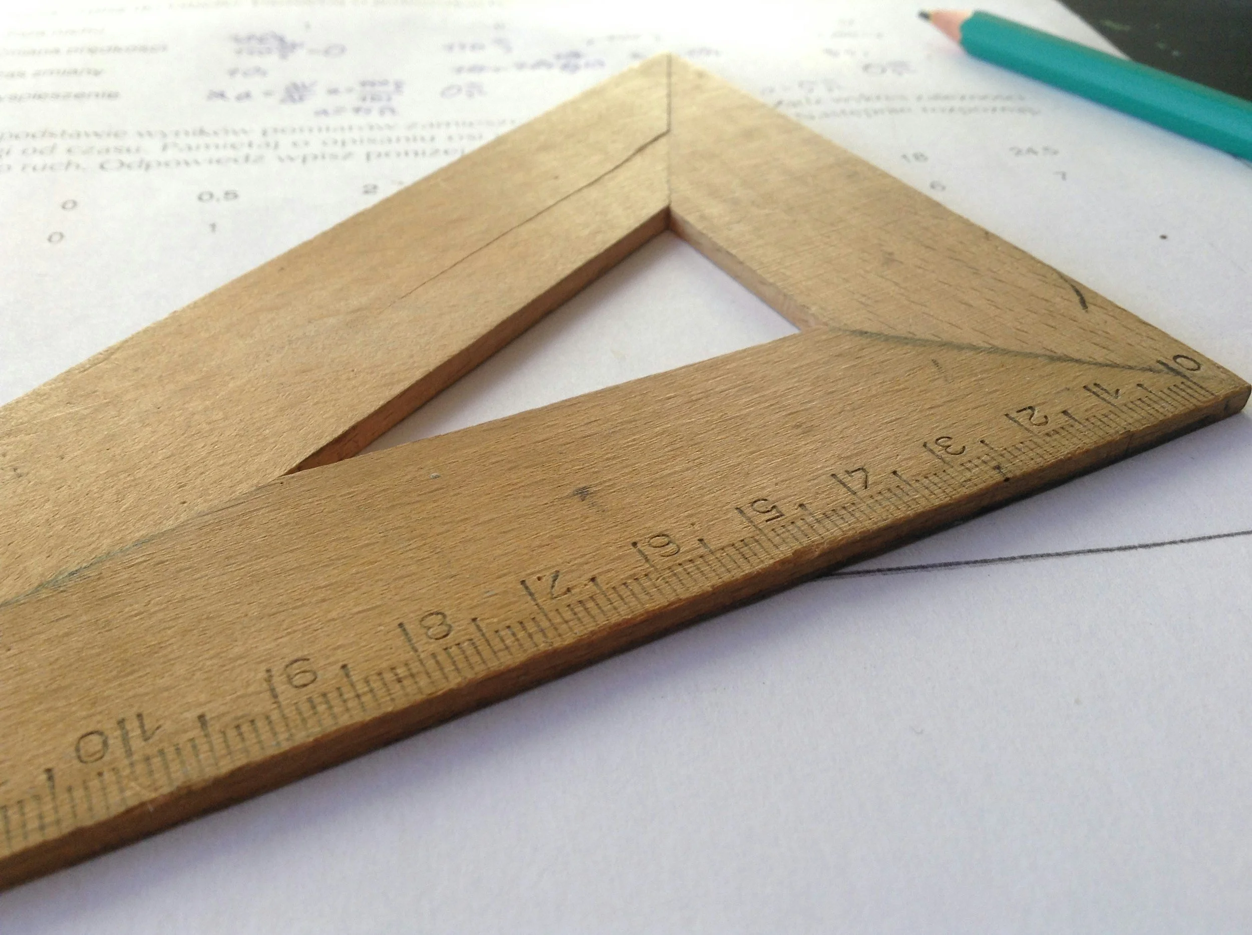 Wooden carpenter's square on a sheet of paper with handwritten notes and a teal pen nearby.