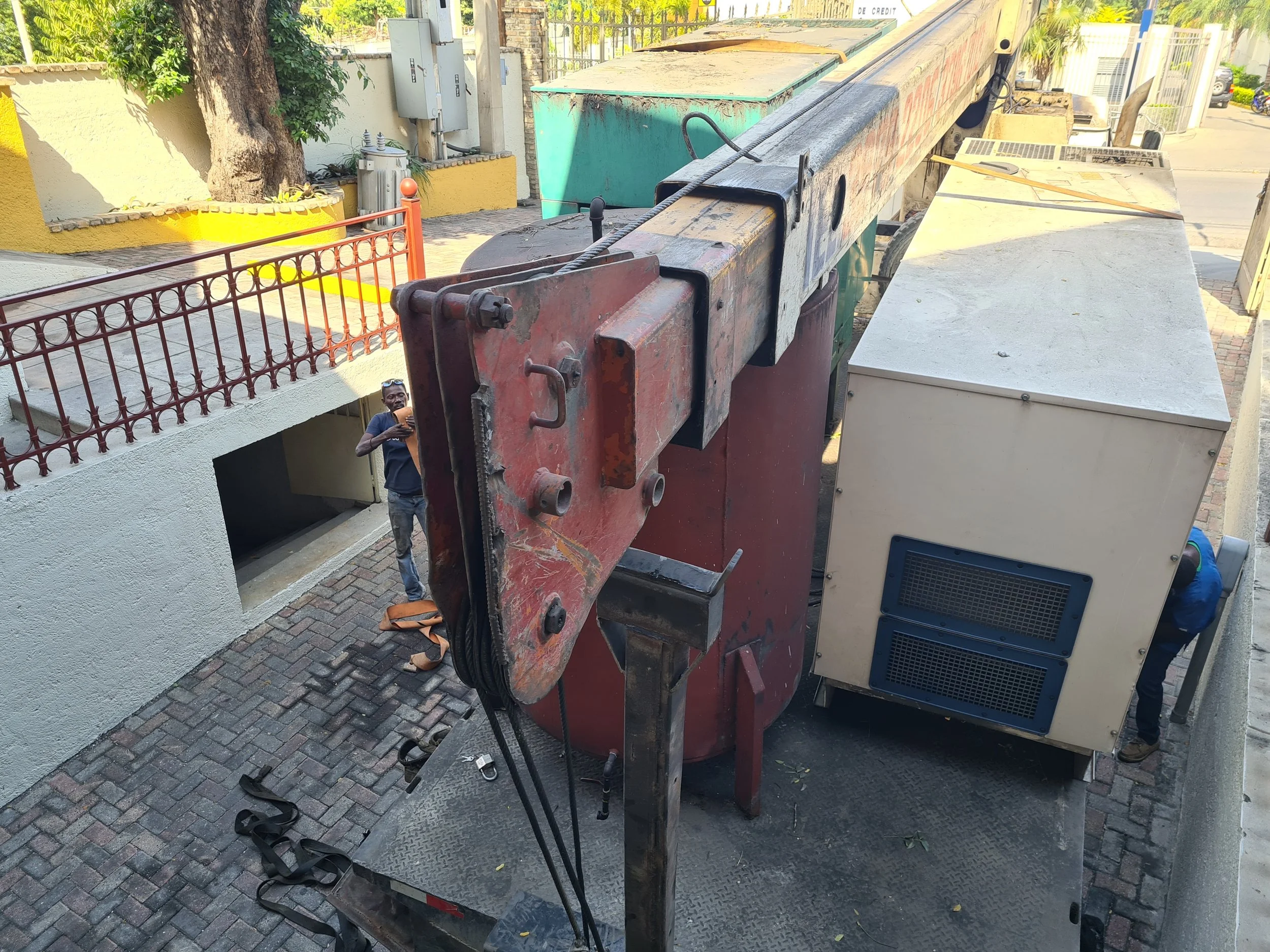 Large construction crane truck with extended boom and control panel, parked on brick driveway next to a sidewalk.