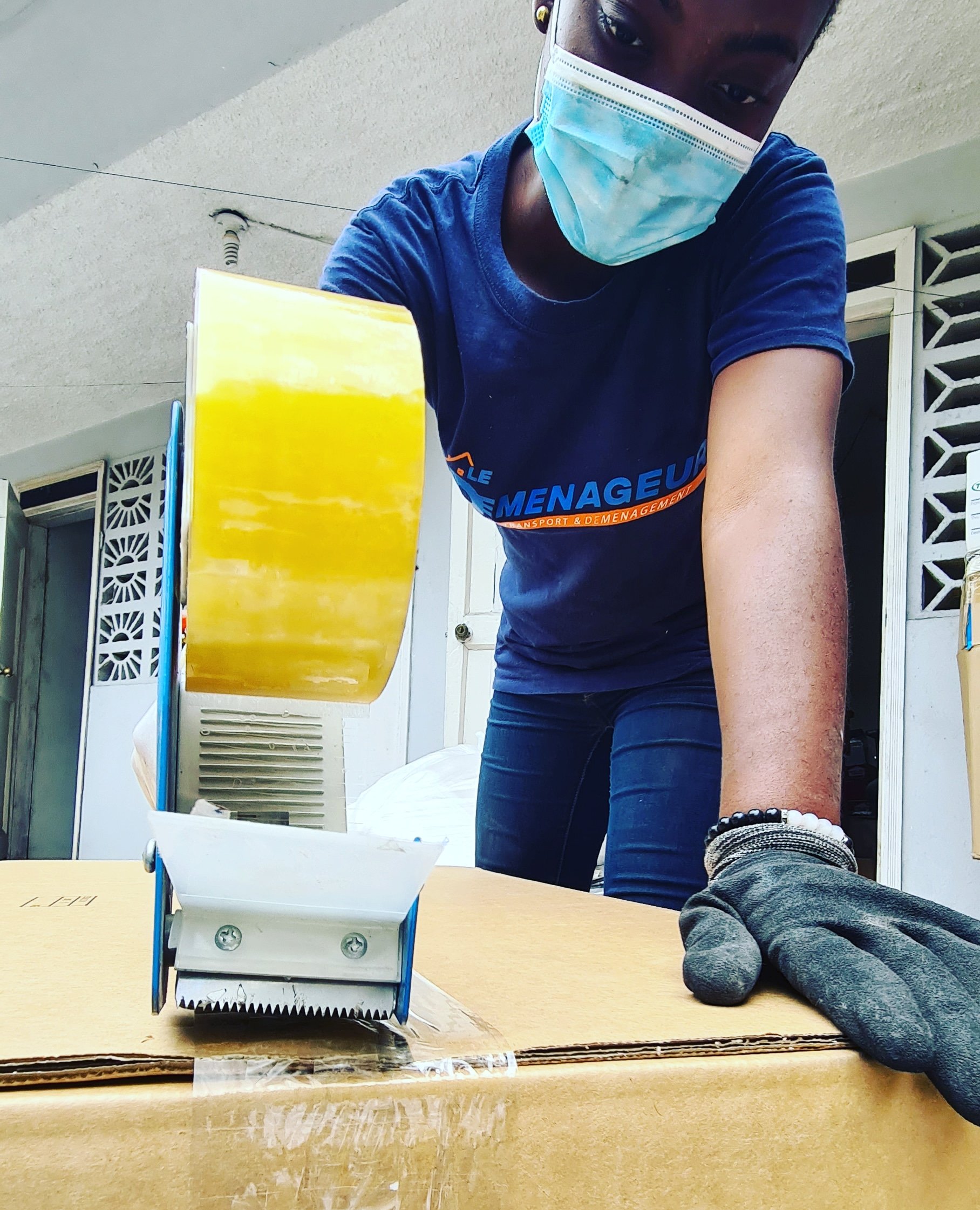 Person in a face mask operating a yellow tape dispenser on a cardboard box.