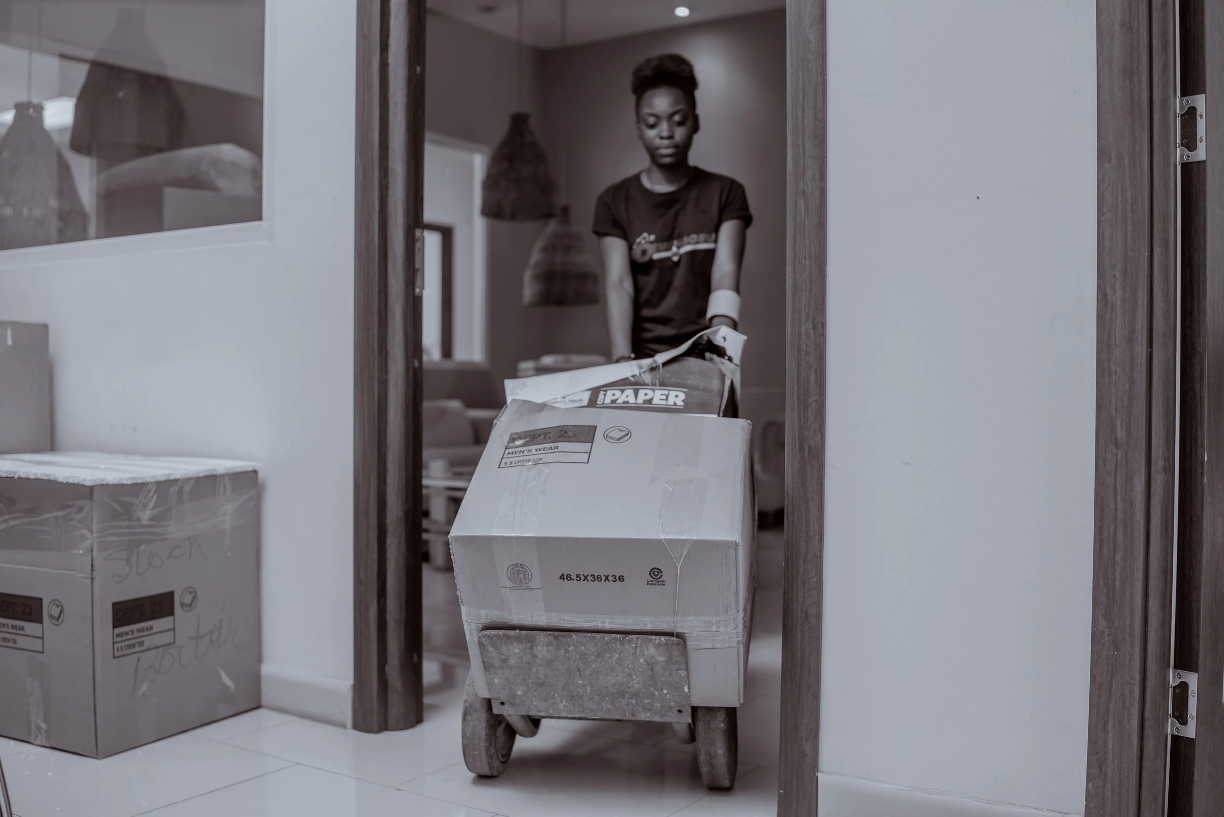A woman with an arm amputation handling a hand truck loaded with boxes in a room.