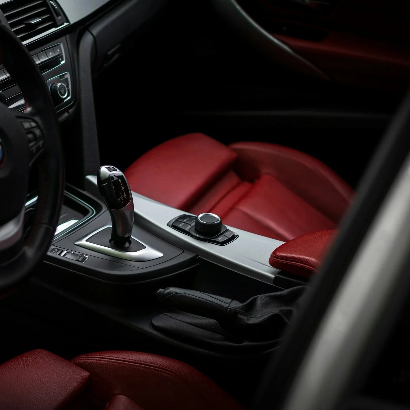 Interior of a car with a gear shift, control knob, red leather seats, and dashboard details.