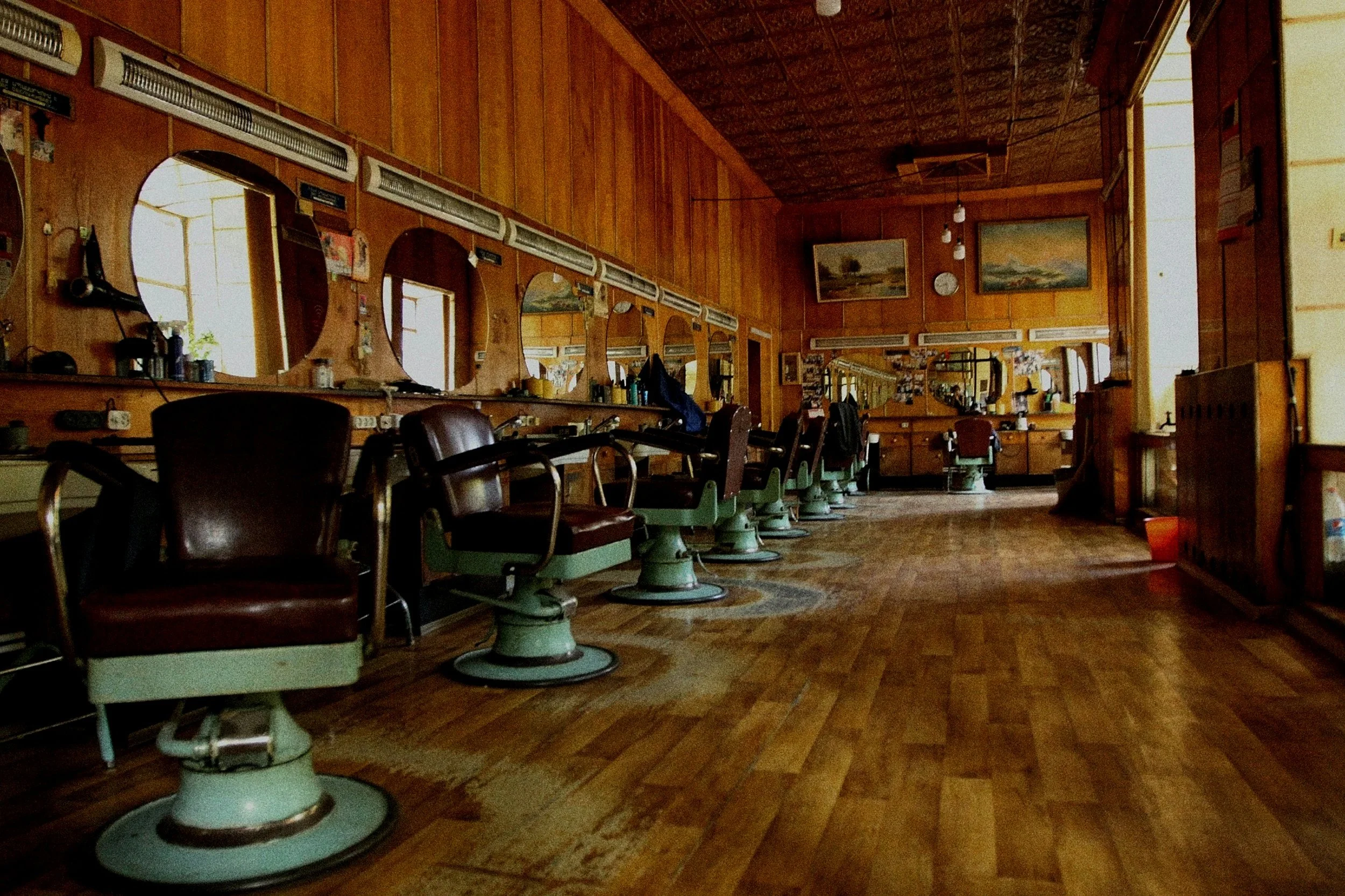 Empty vintage barbershop with wooden walls, old-fashioned barber chairs, large mirrors, and wooden floors.