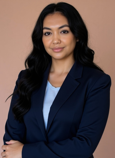 Professional woman with long black hair, wearing a navy blazer and light blue top, standing against a beige background.