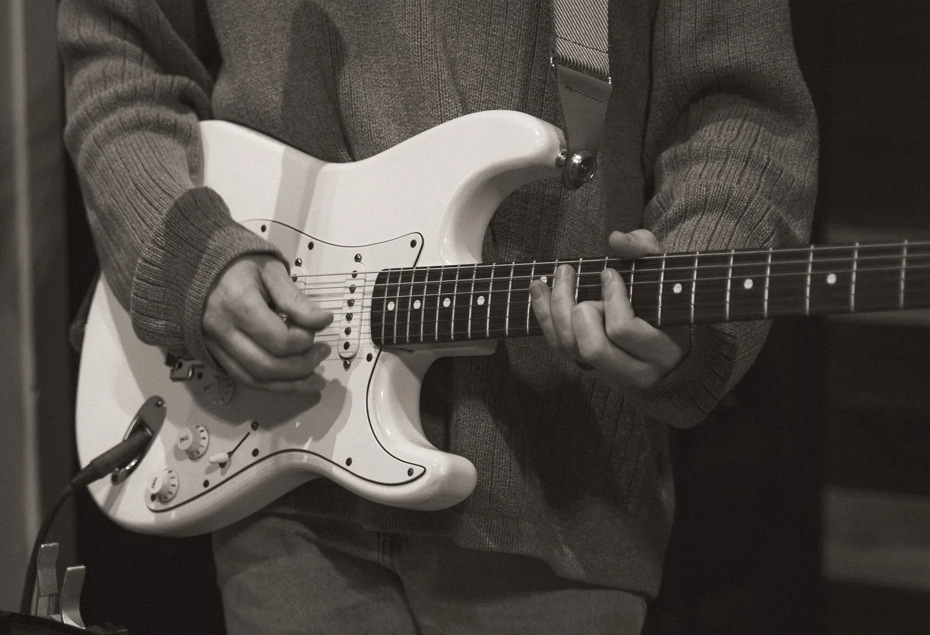 Person playing an electric guitar in worship at church, wearing a gray sweater.