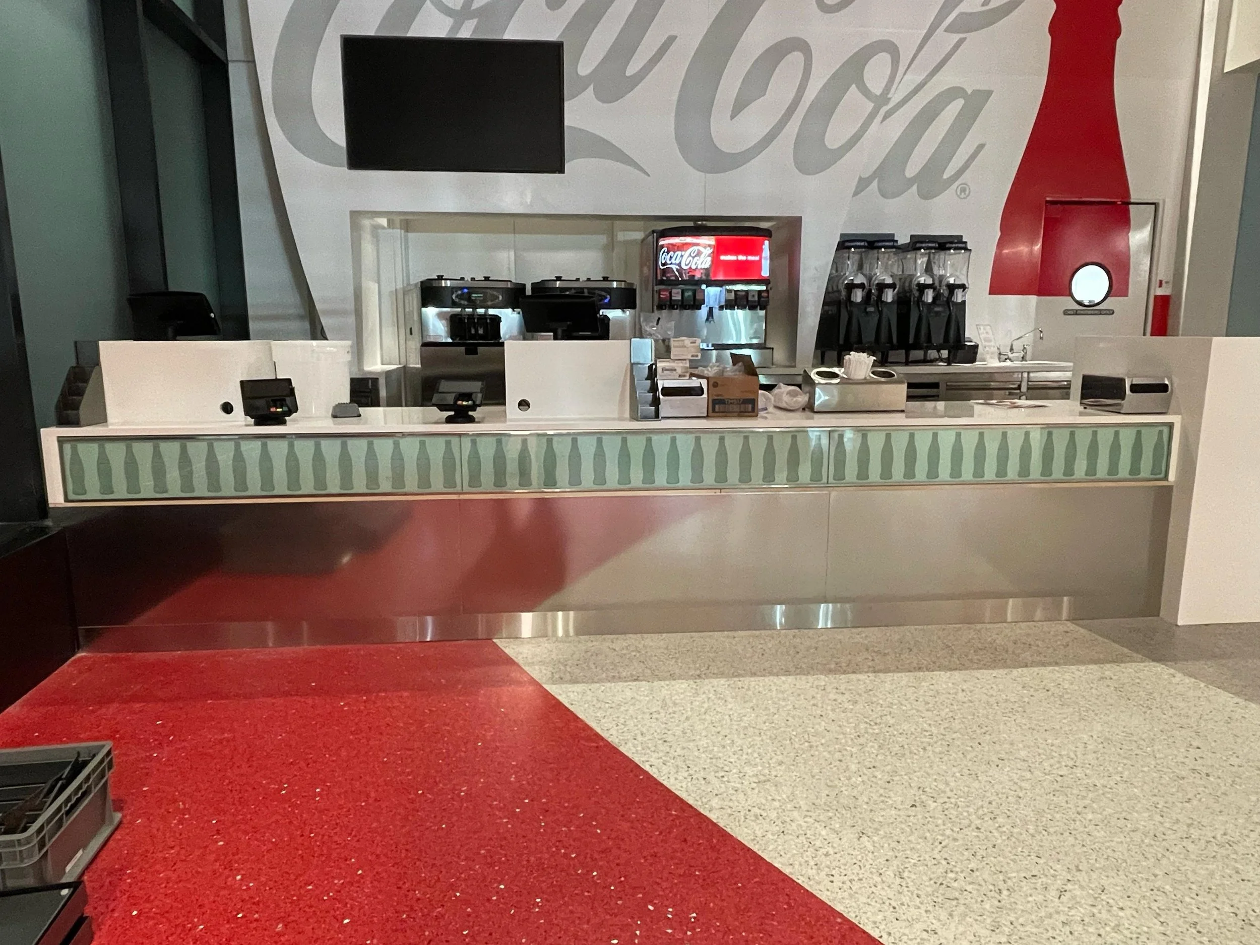 Coca-Cola vending and beverage station with coffee makers, soda dispenser, and glass containers on countertop, in a modern setting.