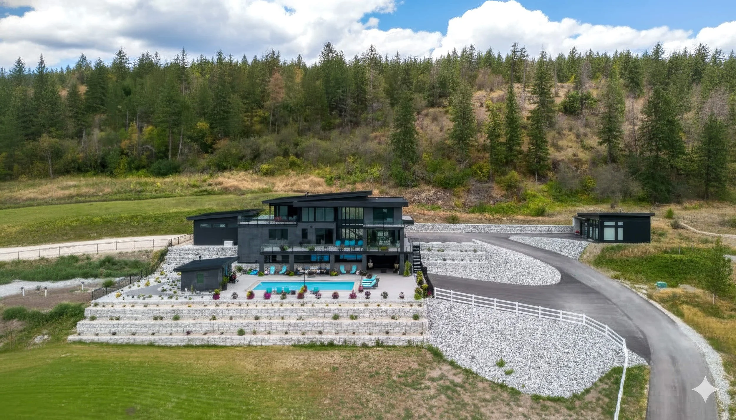 Aerial view of a large modern house with drought-tolerant xeriscape, rock retaining walls and hardscaping, designed and built by Peacock Landscaping in Vernon, BC.
