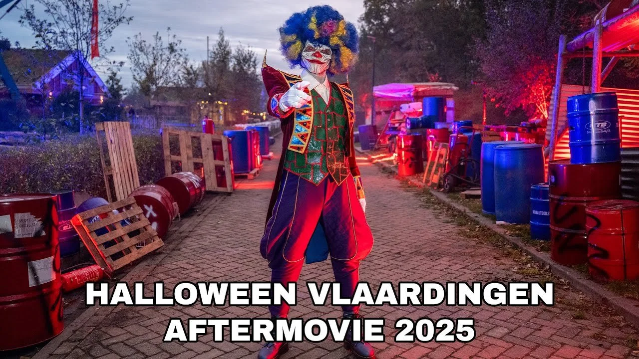 A person dressed as a clown standing on a Halloween-themed set with barrels and crates, surrounded by trees and colorful lights, with text overlay reading 'Halloween Vlaaingen Aftermovie 2025'.