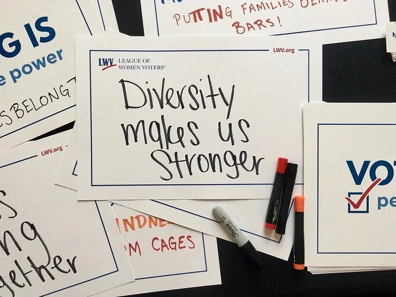 Multiple signs and posters with messages about diversity and voting, including one that says 'Diversity makes us stronger' and others with slogans like 'Putting families first' and 'We belong'.