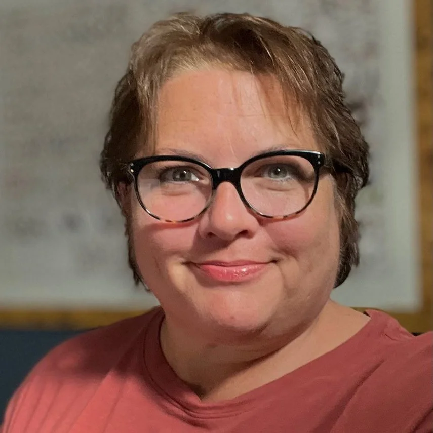 A woman with short brown hair and glasses, smiling at the camera.