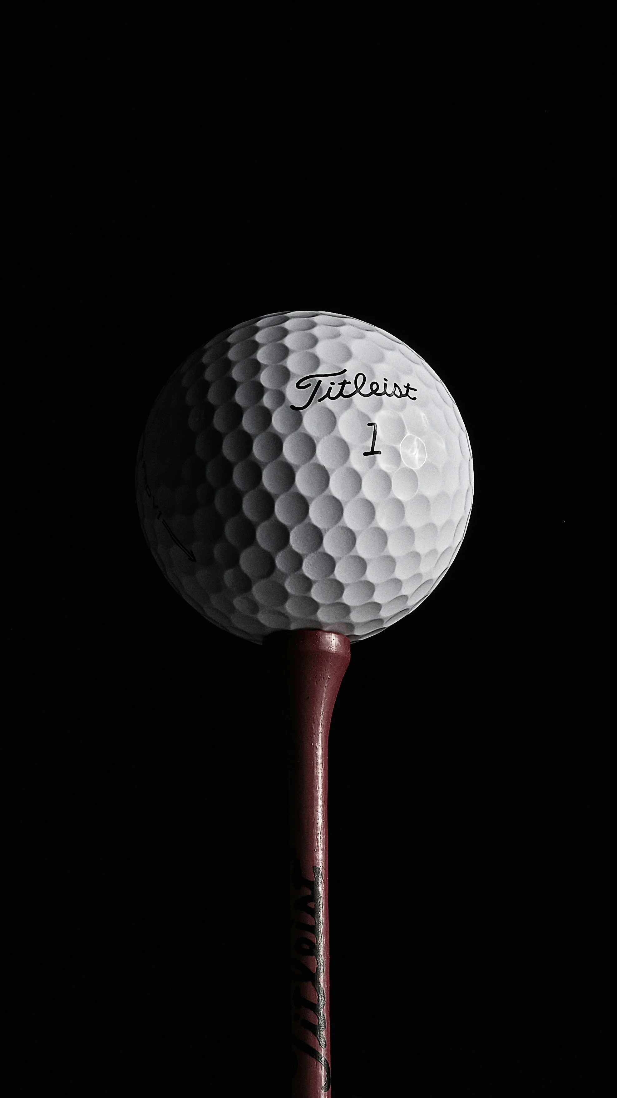A golf ball placed on a pink tee against a black background.