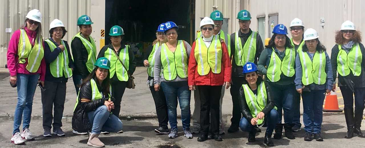 Group of people in safety vests and hard hats standing outside an industrial building.