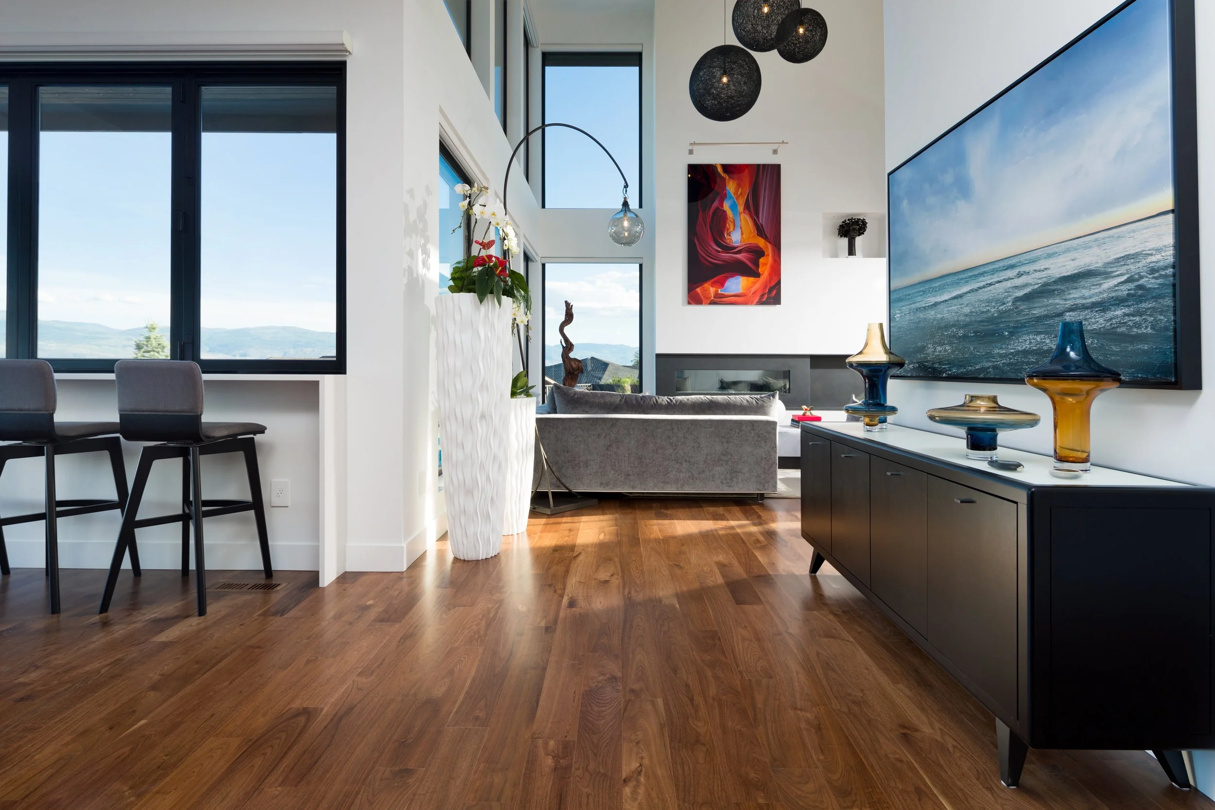 Modern living room with large windows, artwork, and decorative vases on a black cabinet.