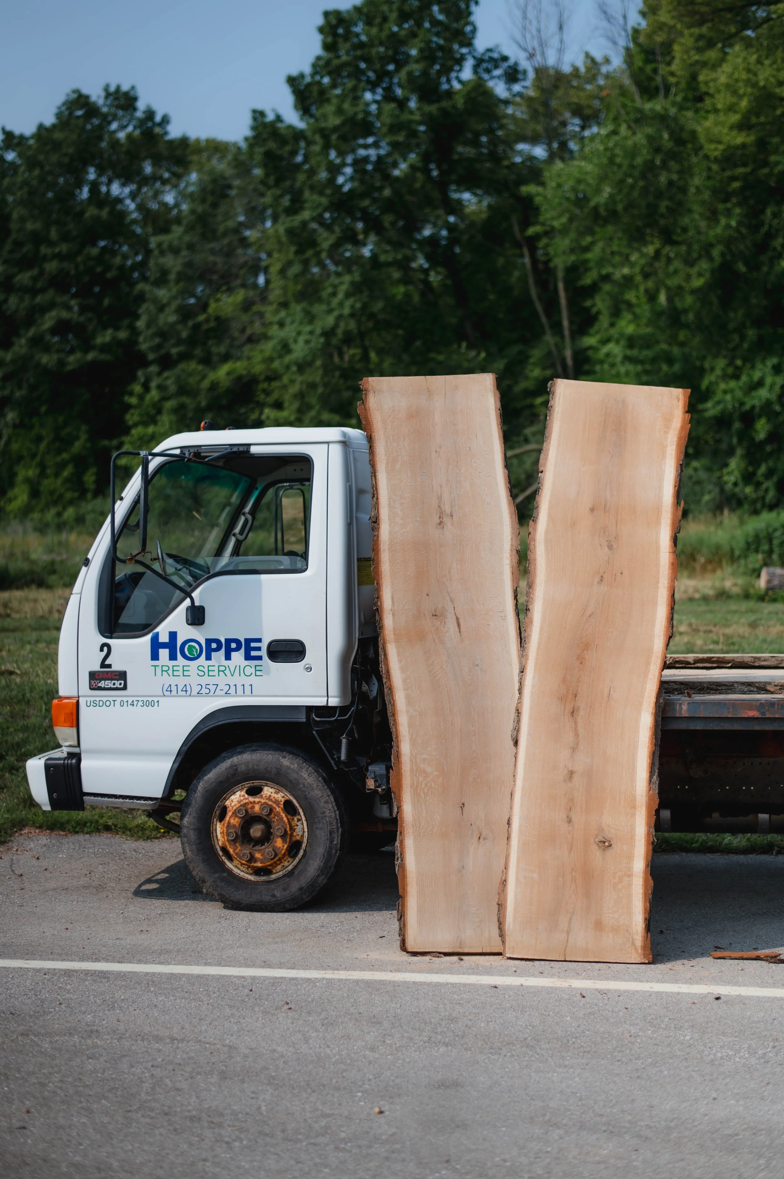 A Hoppe Tree Service truck is parked with two oak slabs leaned upright against the flatbed