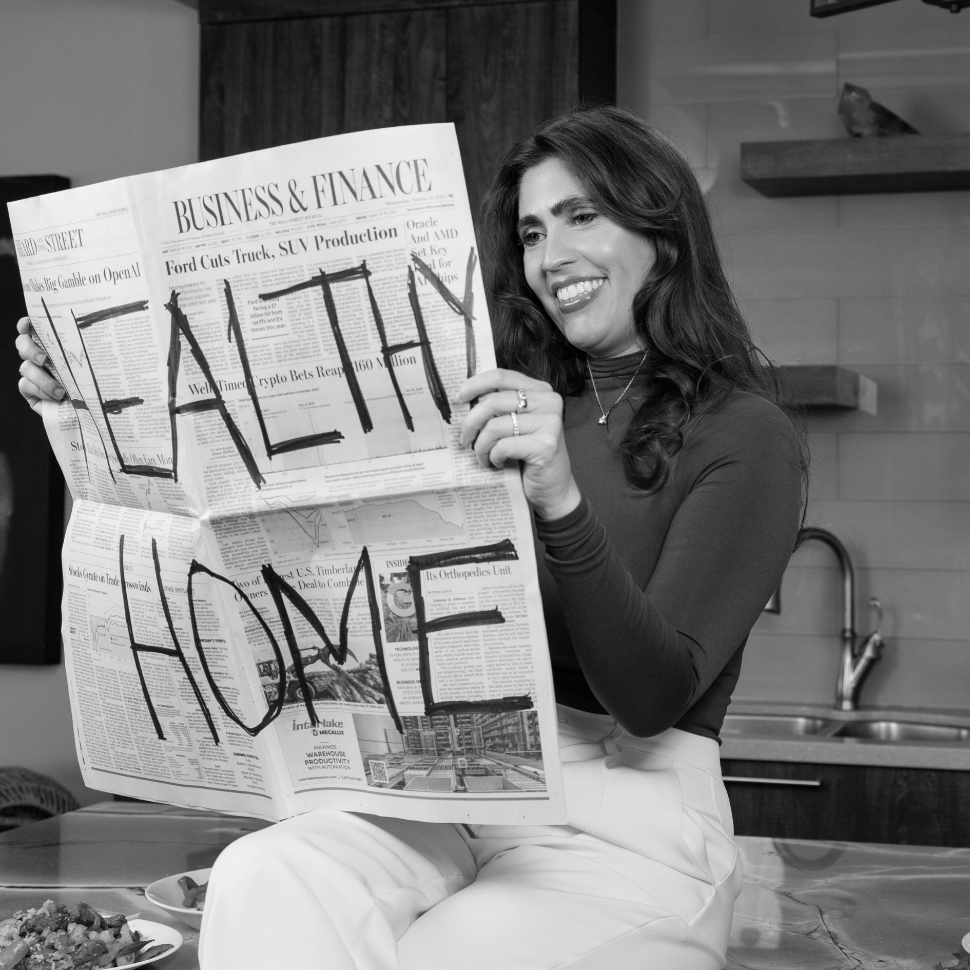 Woman smiling while holding a newspaper with the phrase healthy home written across it in bold lettering