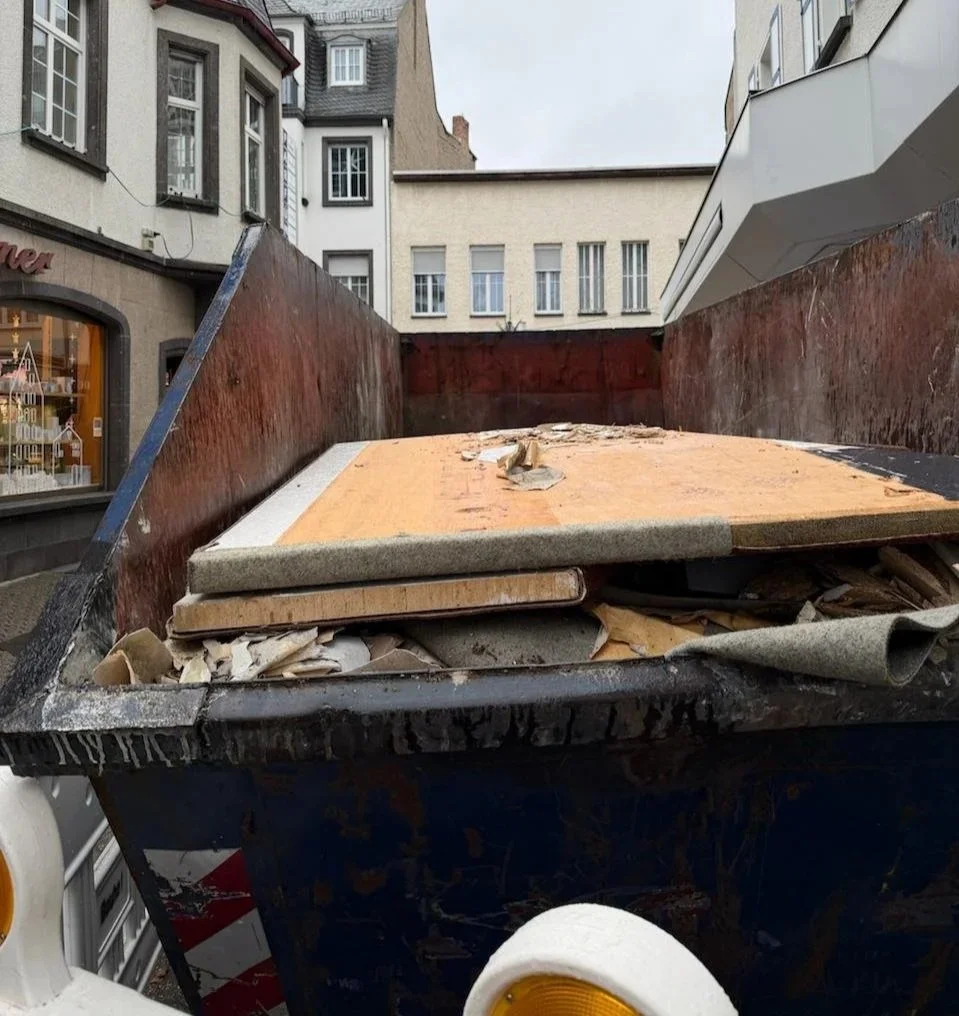 Ein Abfall-Container auf einer Straße, voll mit Müll und alten Holzplatten