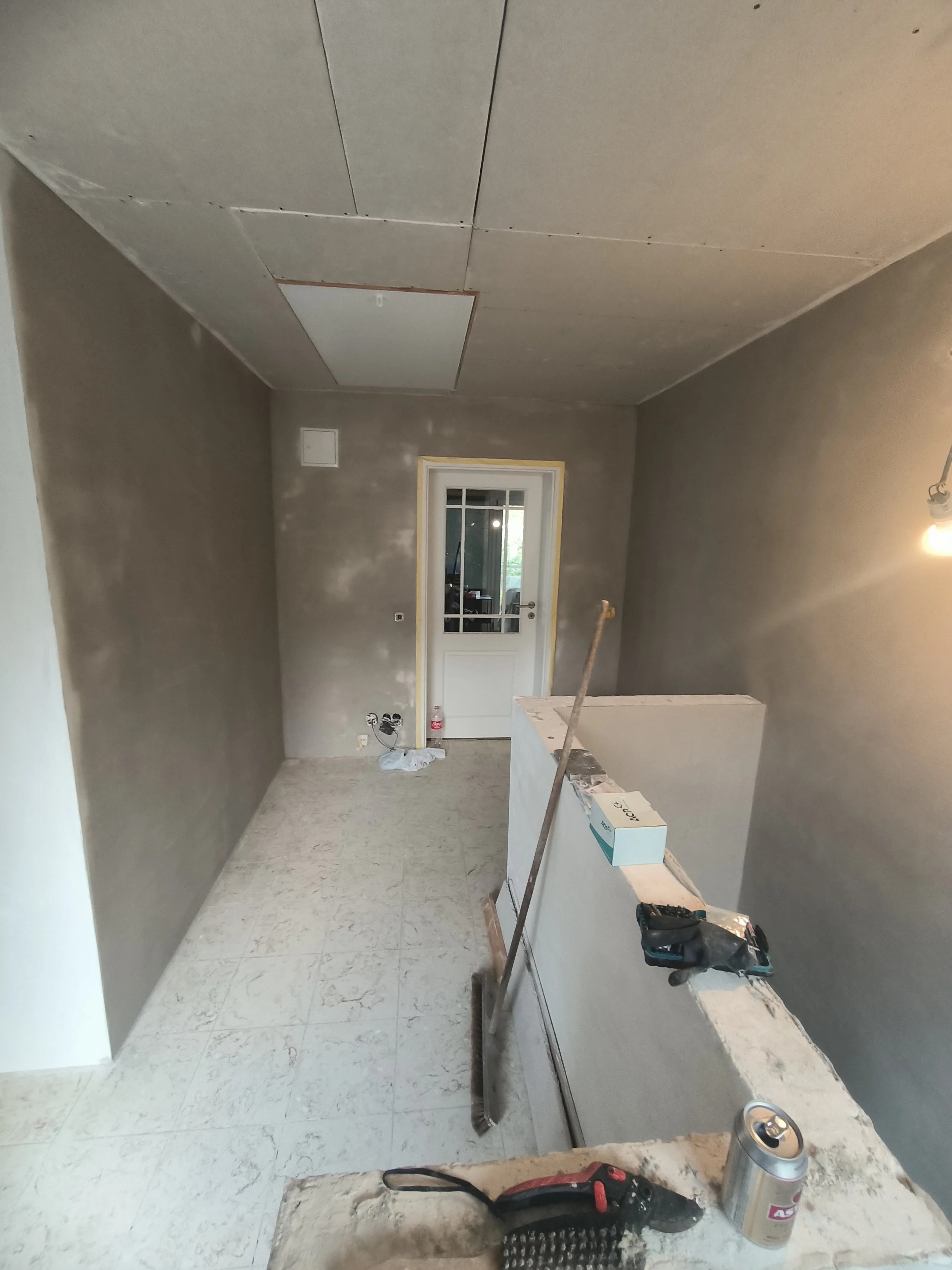 Innenansicht eines Raums in Renovierung, mit unvollendeter Wand und Decke, Werkzeugen und Baumaterialien auf einer Arbeitsfläche.