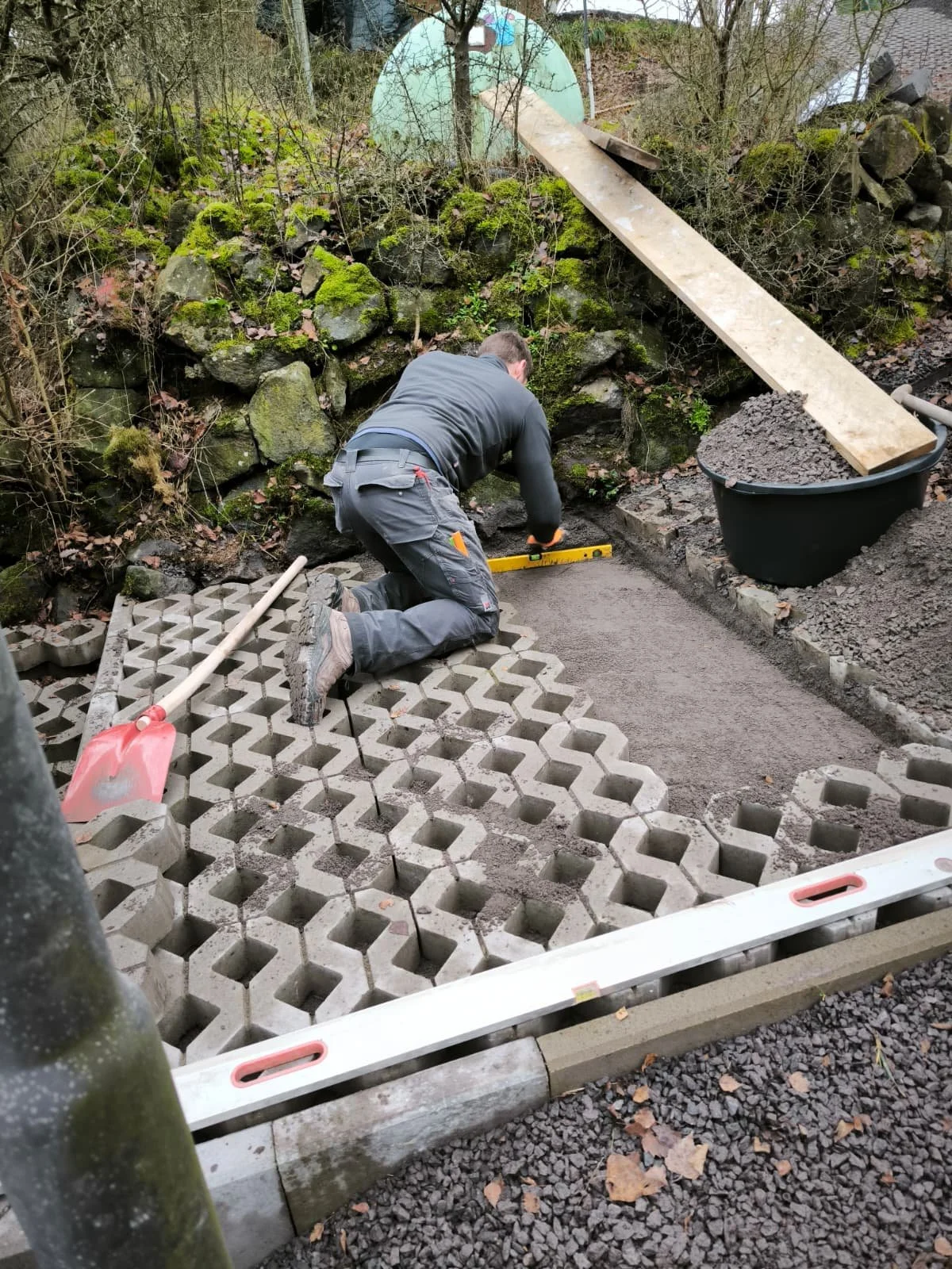Ein Arbeiter legt Pflastersteine. Er arbeitet im Freien, umgeben von Natur mit Steinen und Erde.