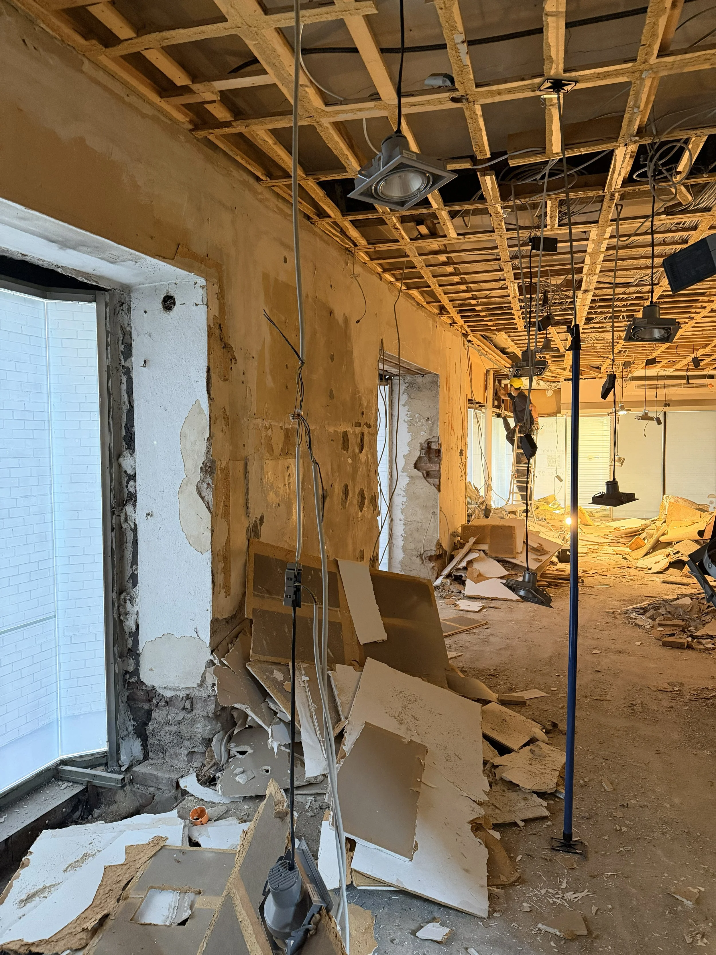 Innenraum eines Gebäudes unter Renovierung, mit zerbrochenen Wänden, Kabel hängen von der Decke, Baustelle mit Schutt und Bauleuchten.