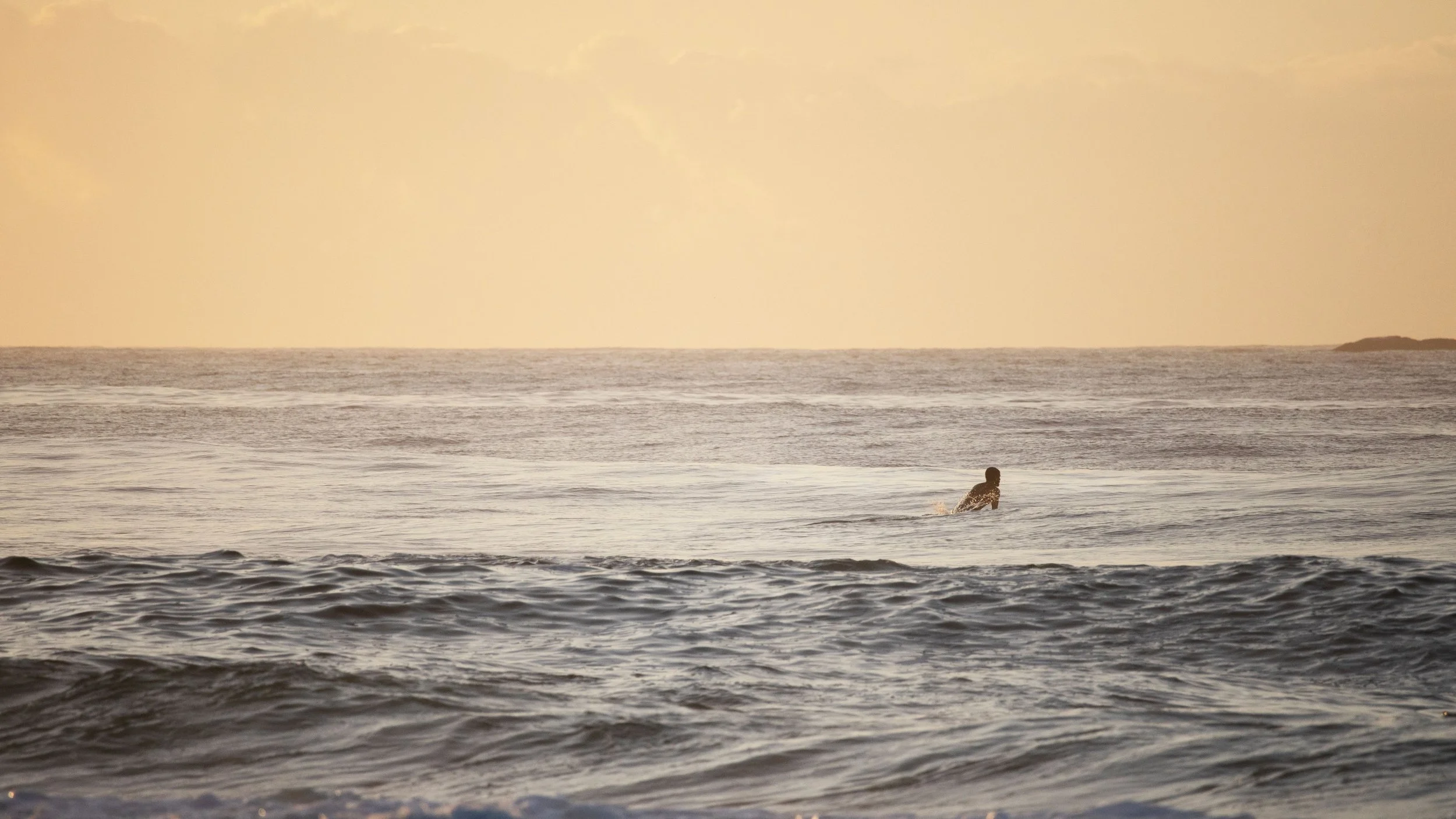 Persona nadando en el mar durante el atardecer o amanecer con cielo nublado y tranquila superficie del agua