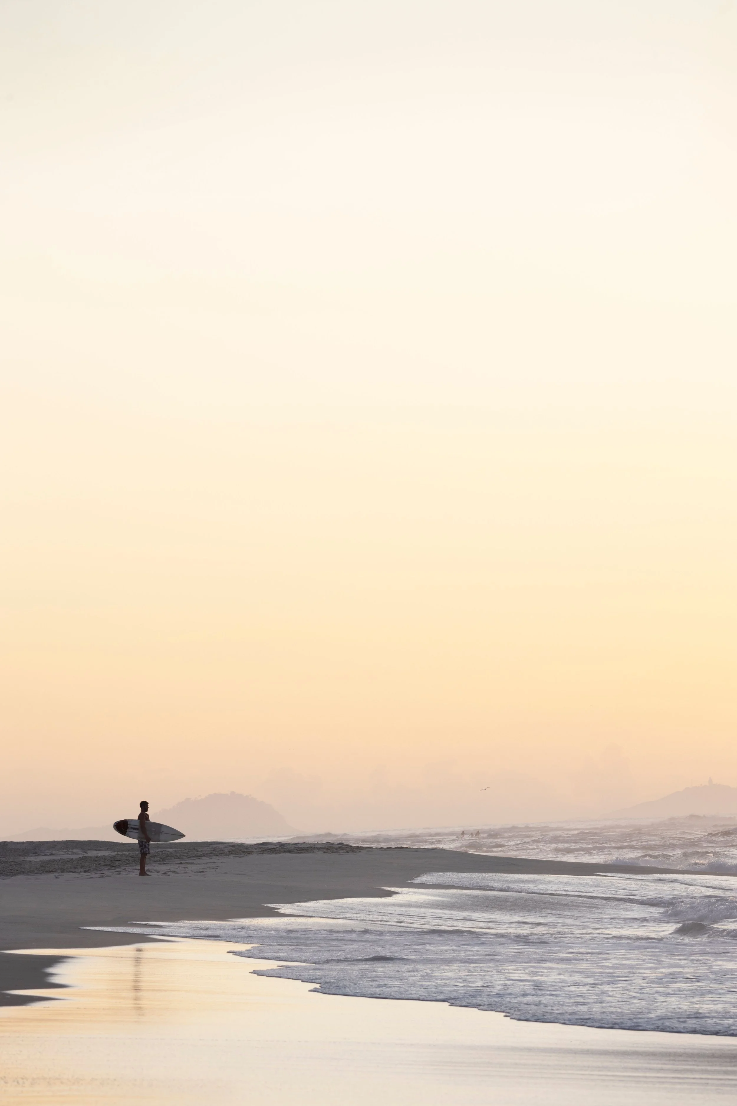Persona de espaldas en la playa con tabla de surf al atardecer, playa de Rio de Janeiro
