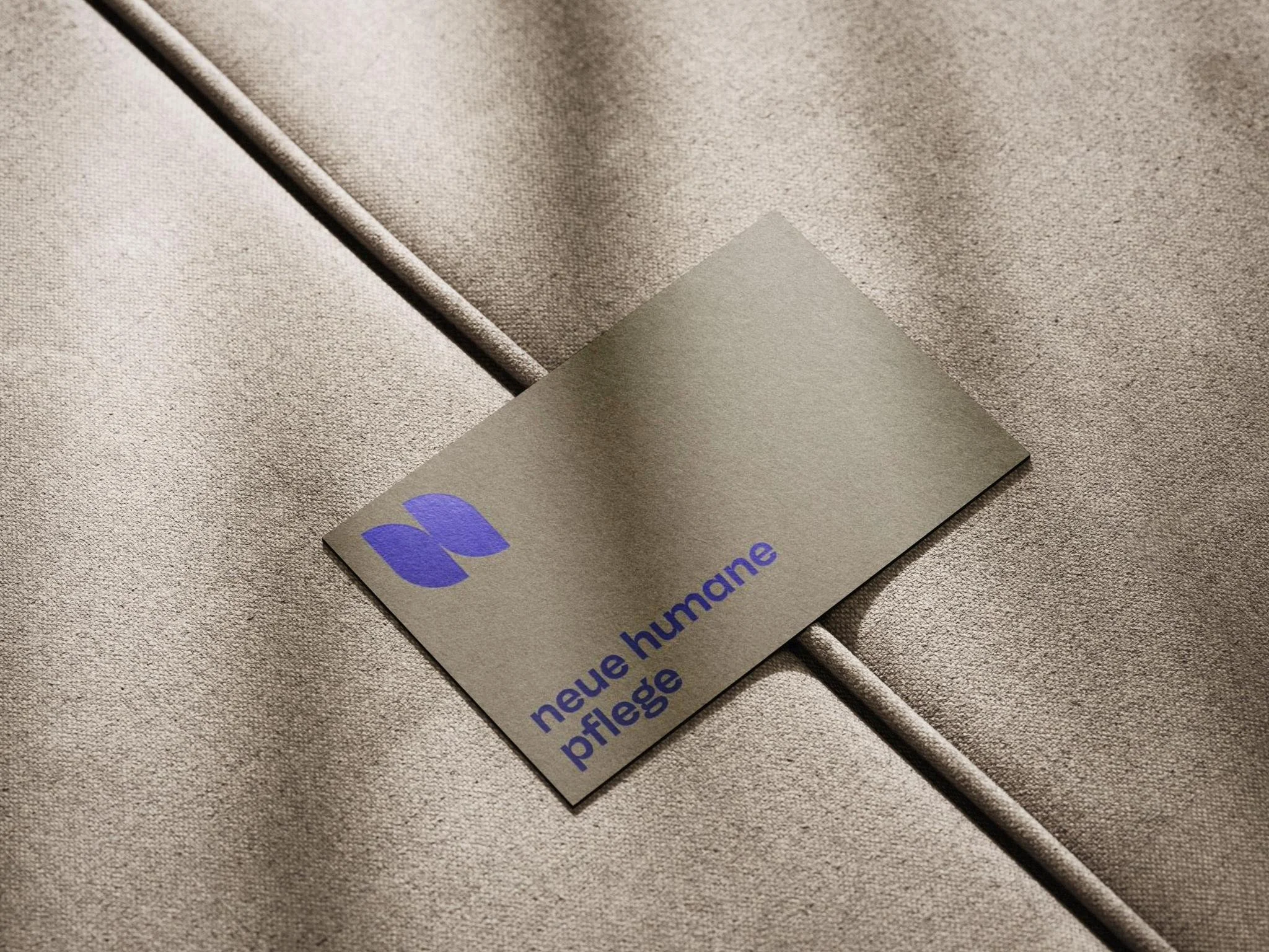 Ein goldfarbenes Stoffetikett mit blauer Schrift und Logo, das auf einem Textilstoff liegt. Das Etikett trägt die Aufschrift 'neue humane pflege'.