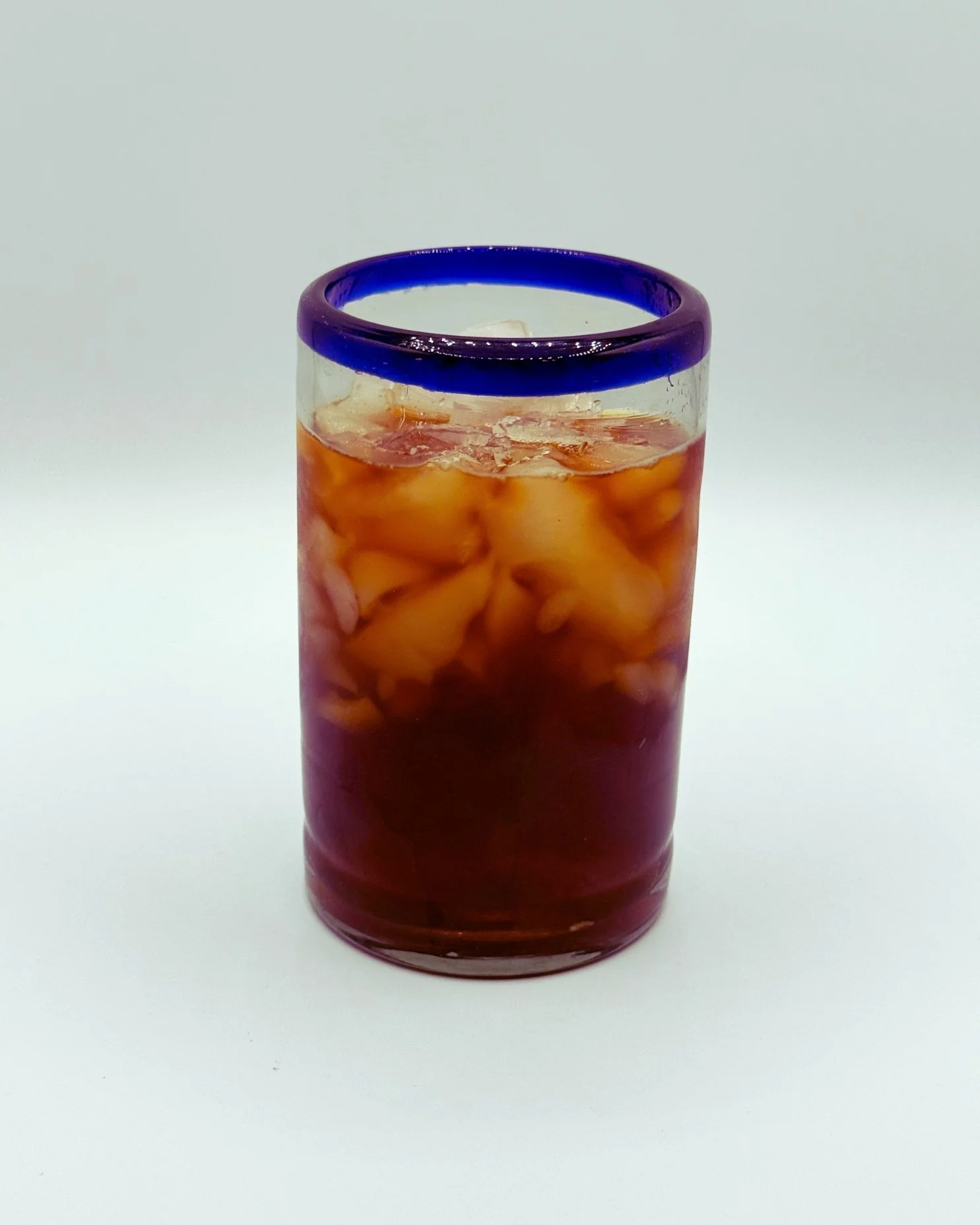 A glass with a blue rim, filled with iced tea and ice cubes.
