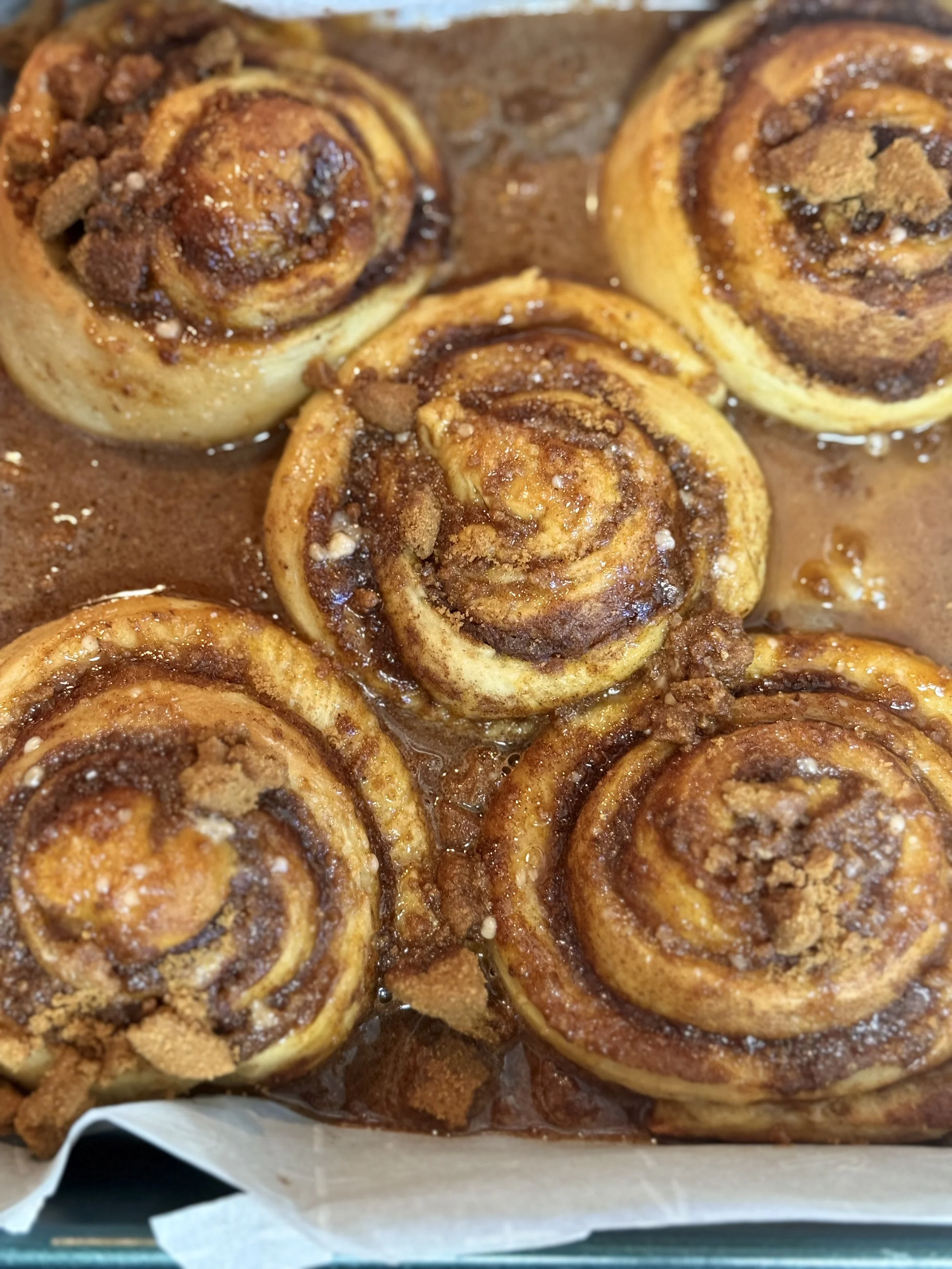 Cinnamon rolls with icing and crumbs in a baking tray.